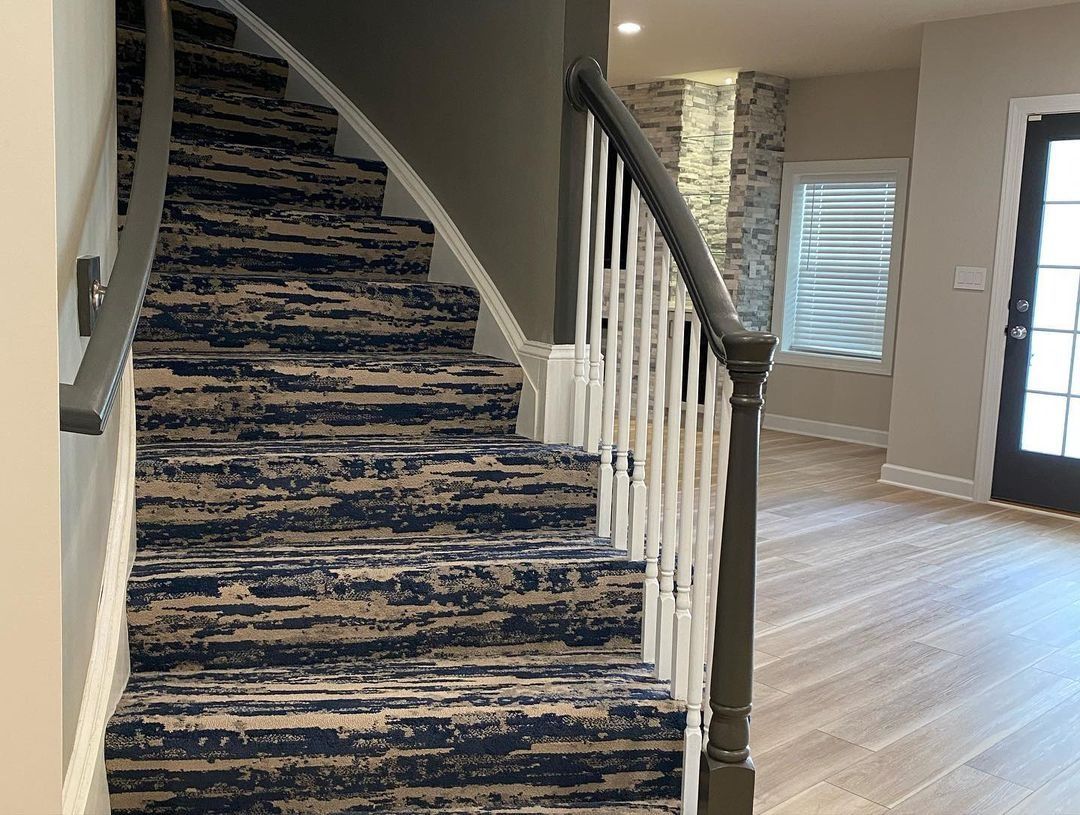 Staircase with patterned carpet, dark railing, white spindles, leading up. Wooden floor visible on the right.