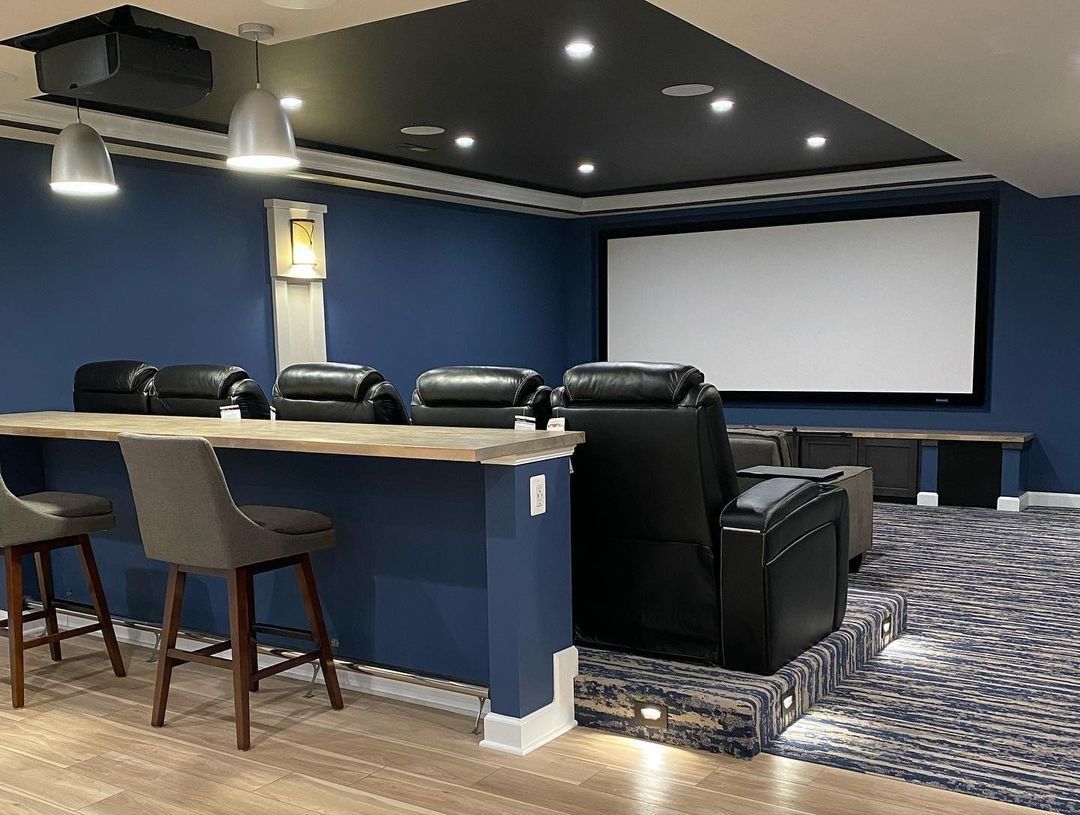 Home theater with tiered seating, blue walls, a screen, and a bar area with stools.