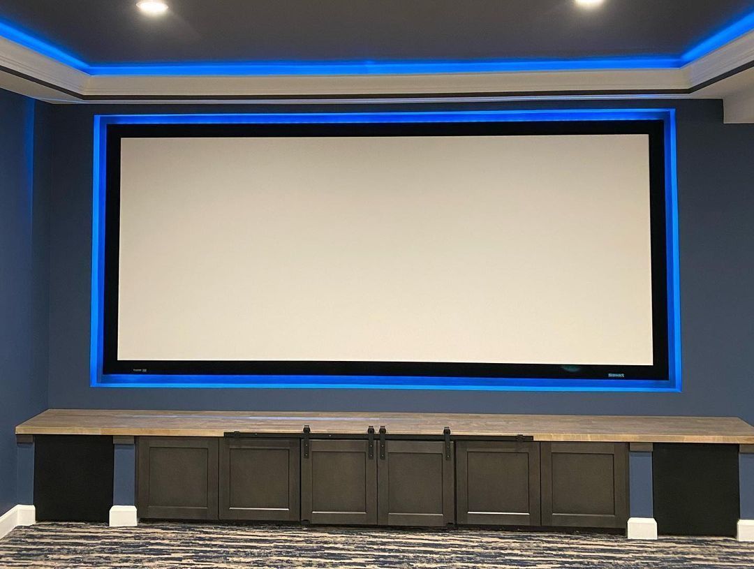 Home theater with a large screen, blue accent lighting, and gray cabinets.