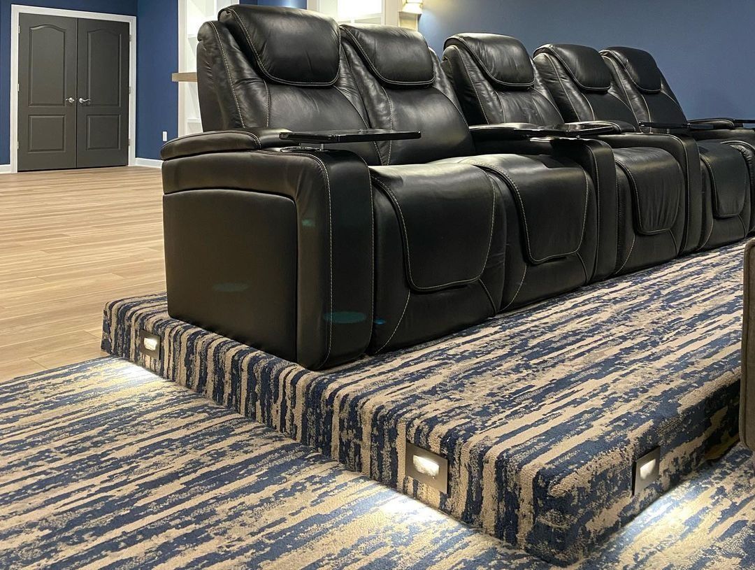 Row of black leather theater seats on a carpeted platform with built-in lights, in a home theater.