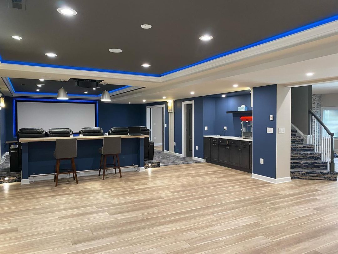 Finished basement with home theater setup: projector, screen, bar with stools, and kitchen area.