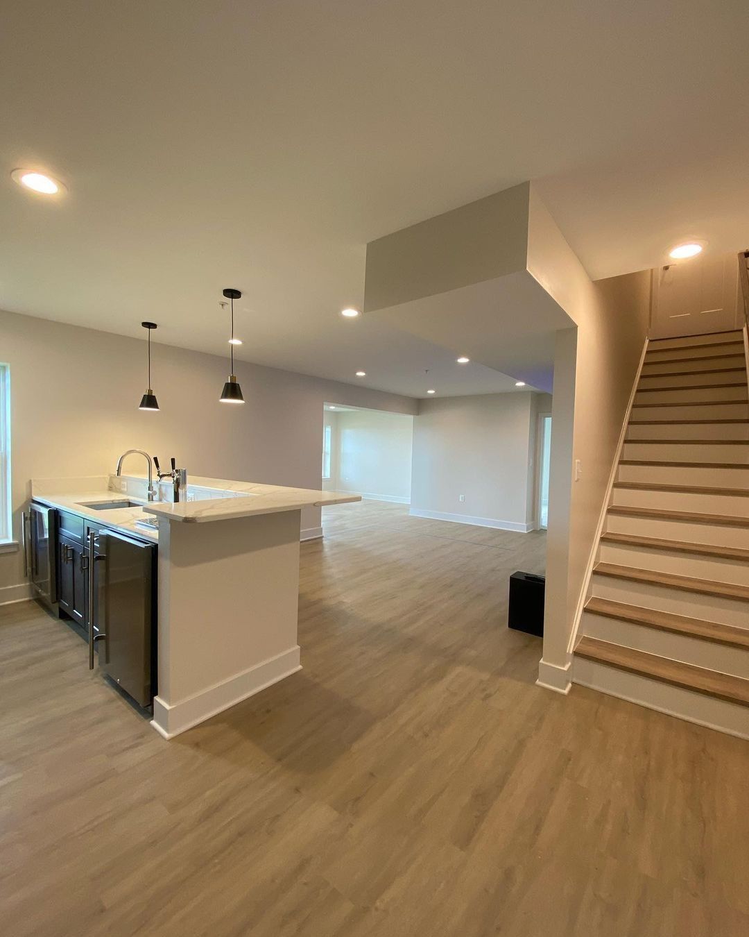 Open-concept kitchen and living area with island, stainless steel appliances, and staircase.