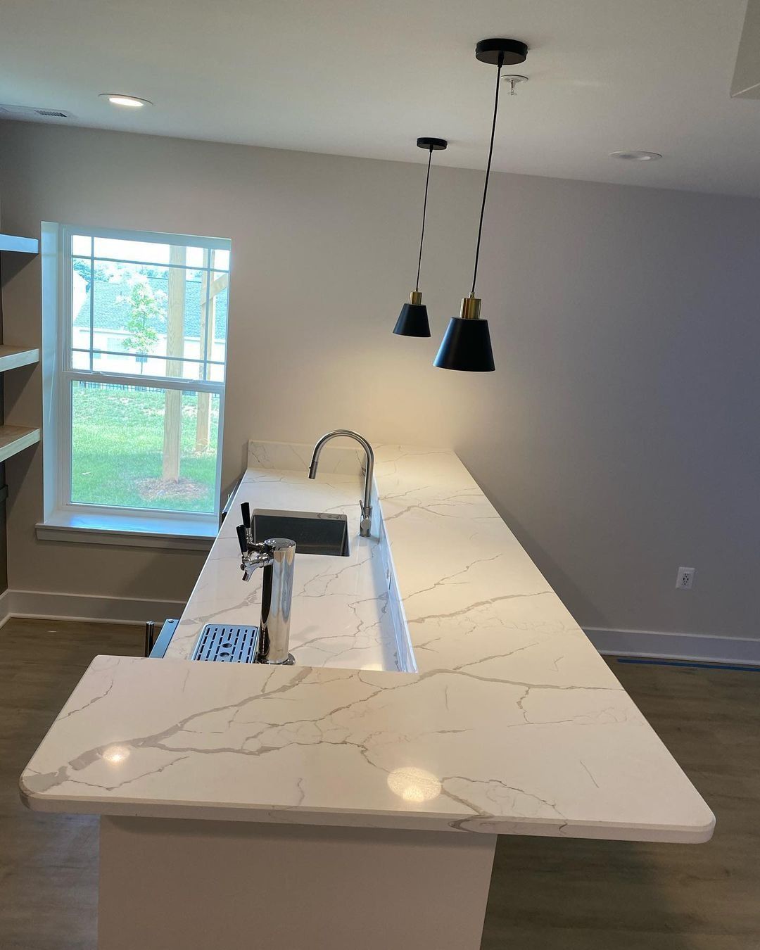 Kitchen island with white countertops, faucet, and pendant lights. A window is in the background.
