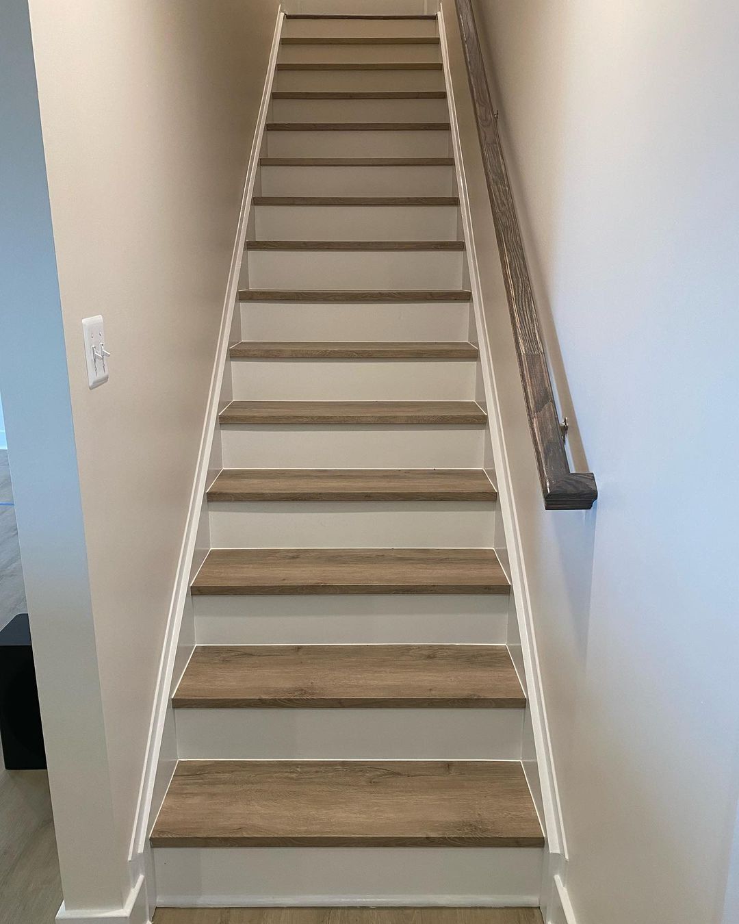 Staircase with wooden steps and white risers, beige walls, and a wooden handrail.
