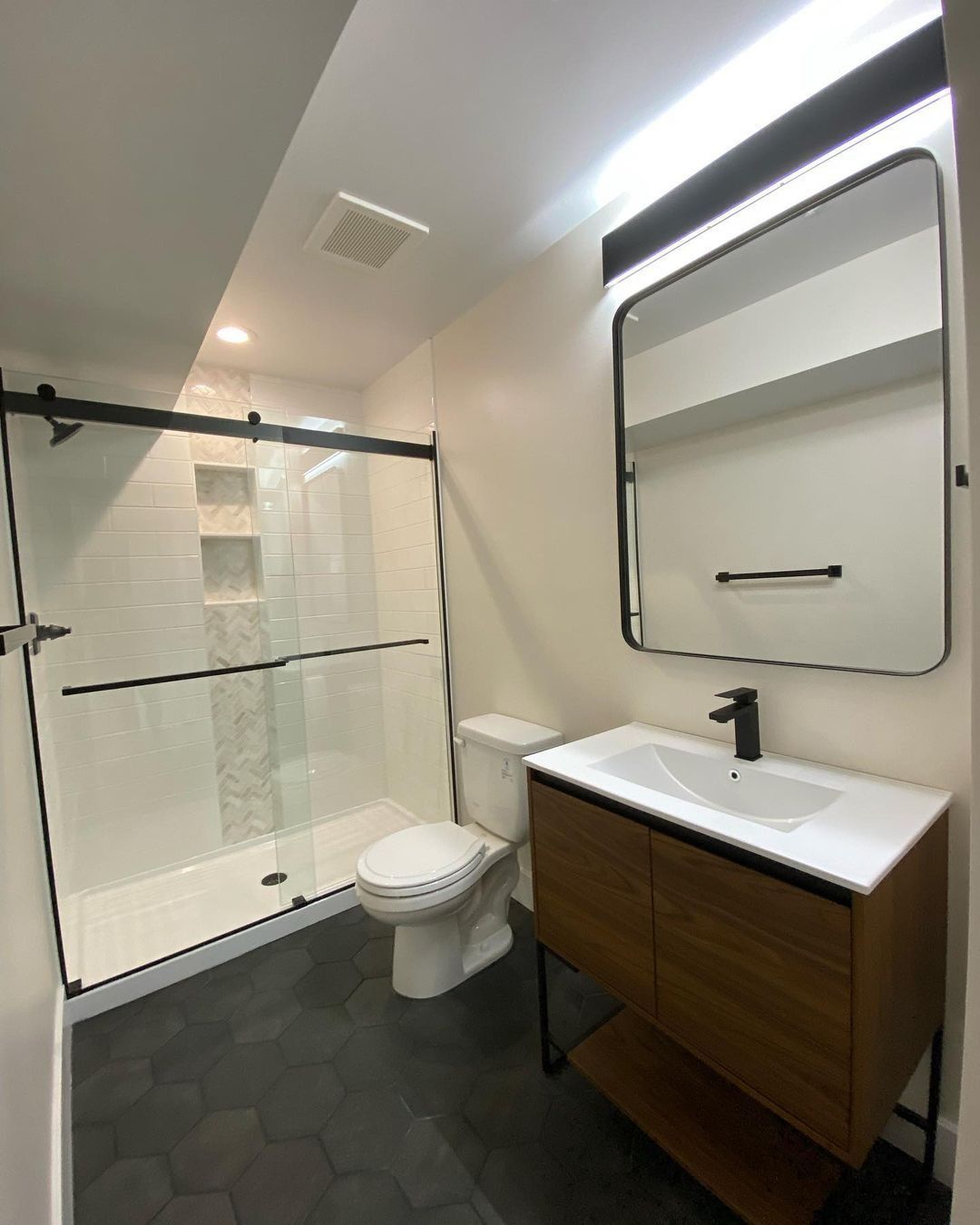 Modern bathroom with glass shower, floating vanity, toilet, and black hex floor.