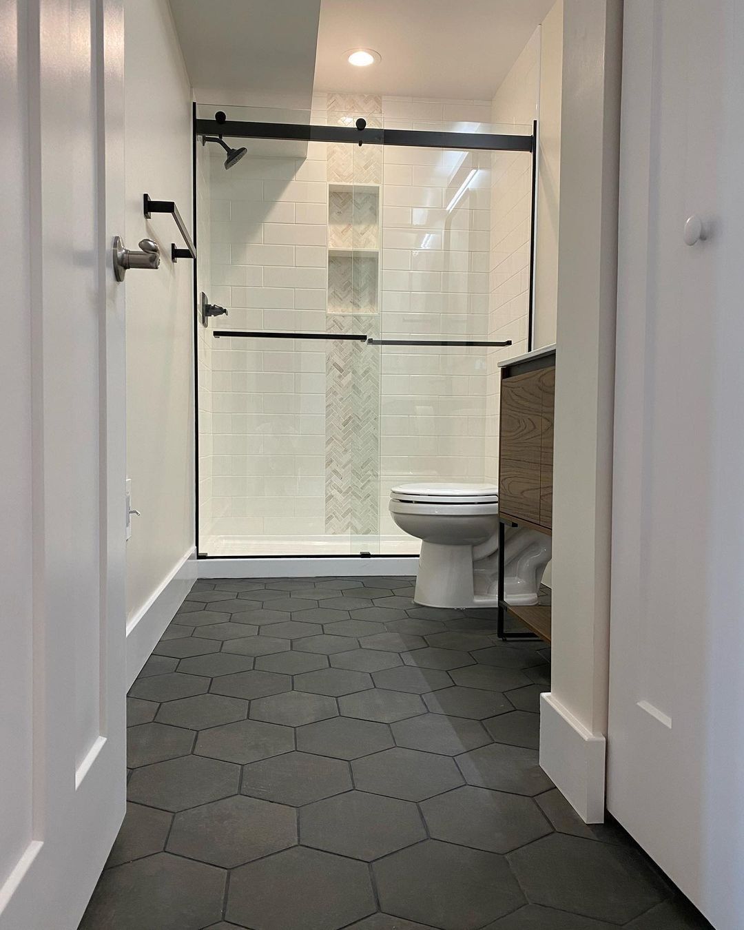 Bathroom with black hexagon tile floor, white walls, glass shower, and a toilet.