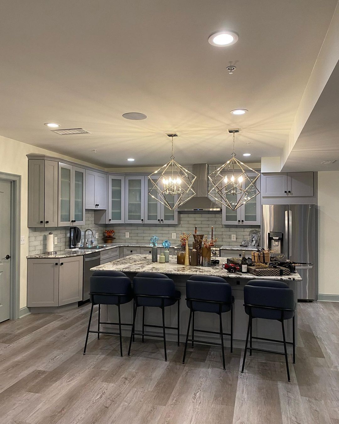 Modern kitchen with a gray island and cabinets, stainless steel appliances, and four black bar stools.