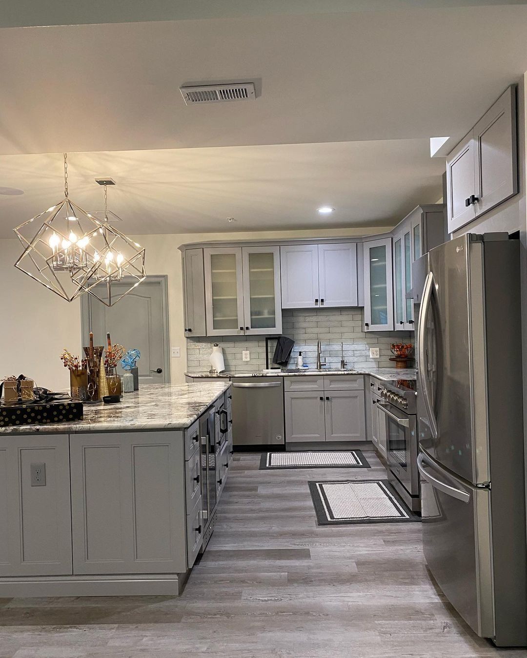Gray and white kitchen with island, stainless steel appliances, and wood-look flooring.