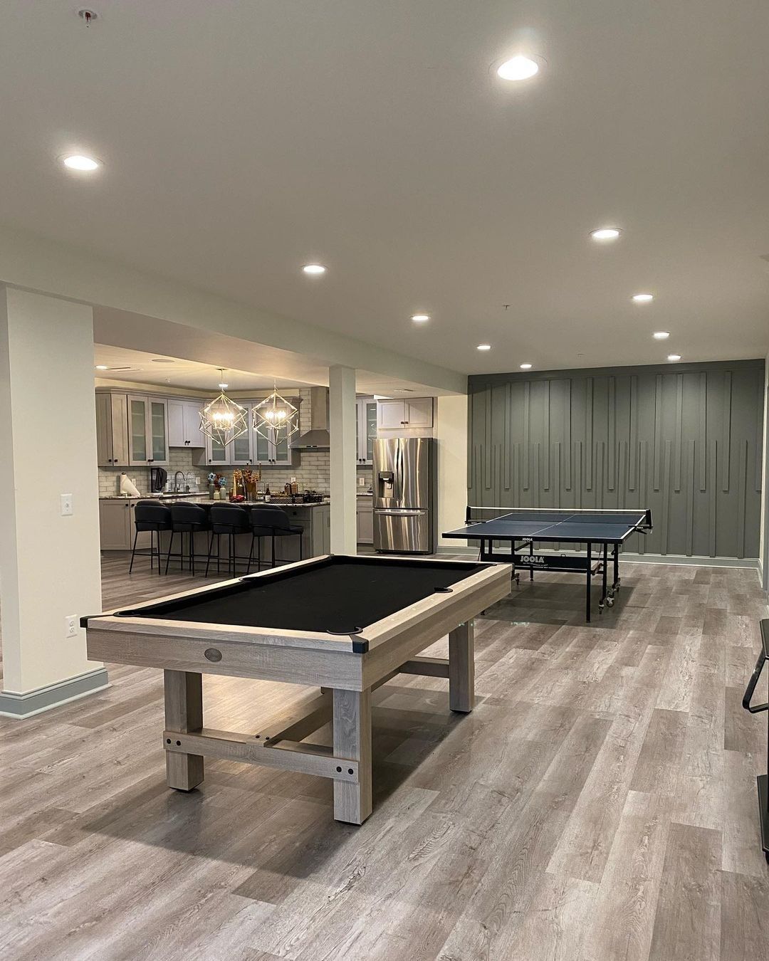 Pool table and ping pong table in a finished basement with kitchen and storage cabinets.
