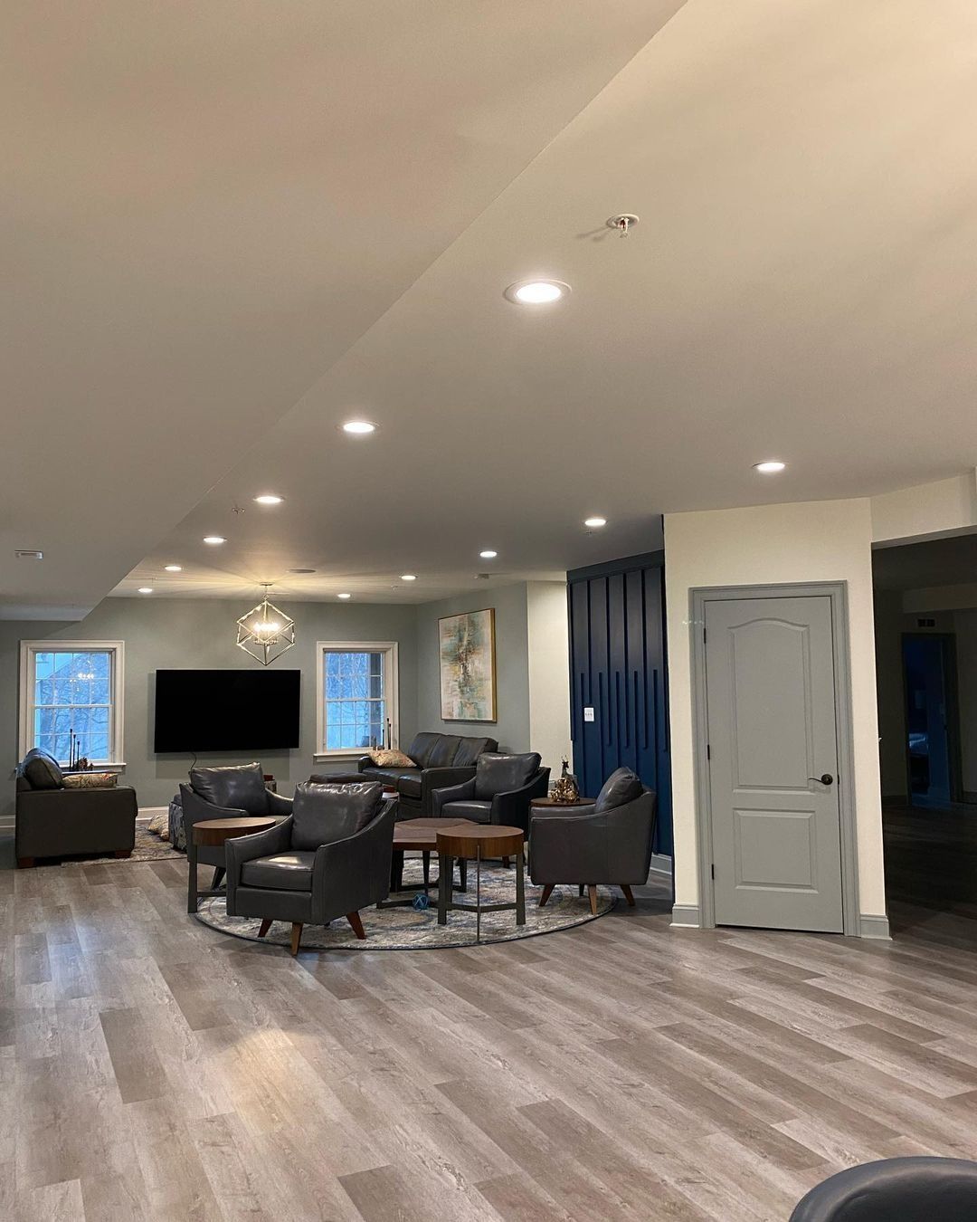 Spacious living area with seating, TV, and wood-look flooring. Light walls, recessed lighting, and a blue accent wall.