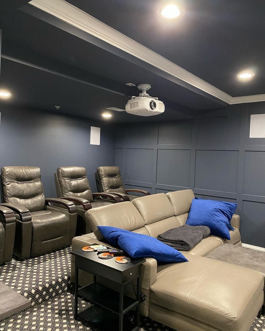 Home theater with dark blue walls, recliners, and a sectional sofa. Projector is mounted on the ceiling.