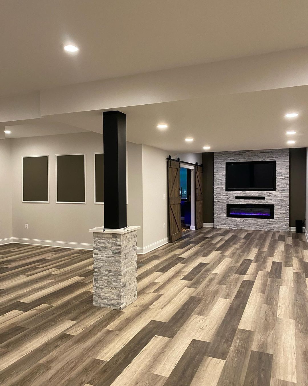 Finished basement with stacked stone pillar, gray walls, wood-look flooring, and a fireplace.