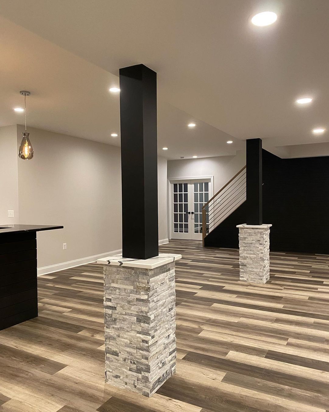 Basement with black column on stone base, wood floor, stairs, and door.
