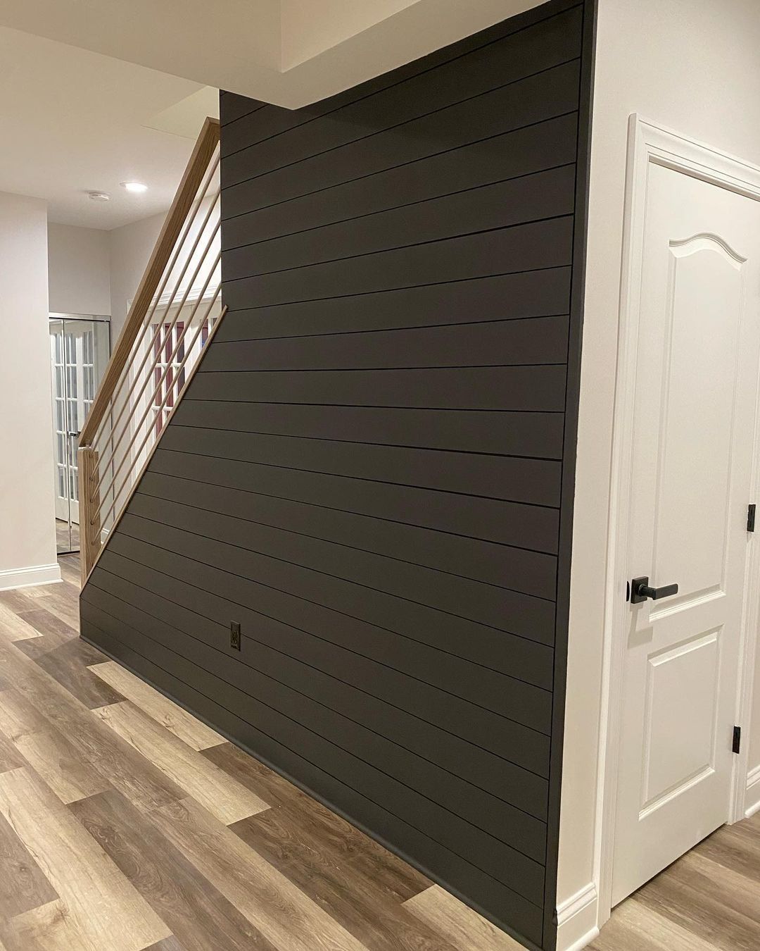 Dark gray shiplap accent wall next to a white door. Wooden staircase with wood and metal railing.