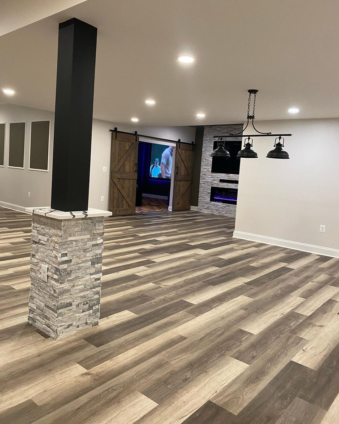 Spacious finished basement with wood-look flooring, stone-faced columns, and a fireplace. Sliding barn doors lead to another room.