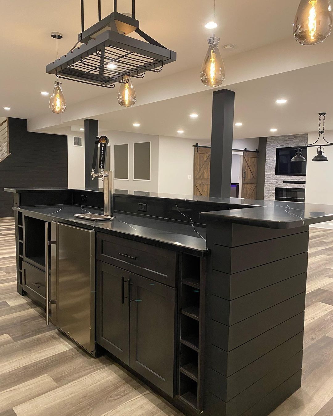 Dark gray basement bar with wine rack and tap, under pendant lights.