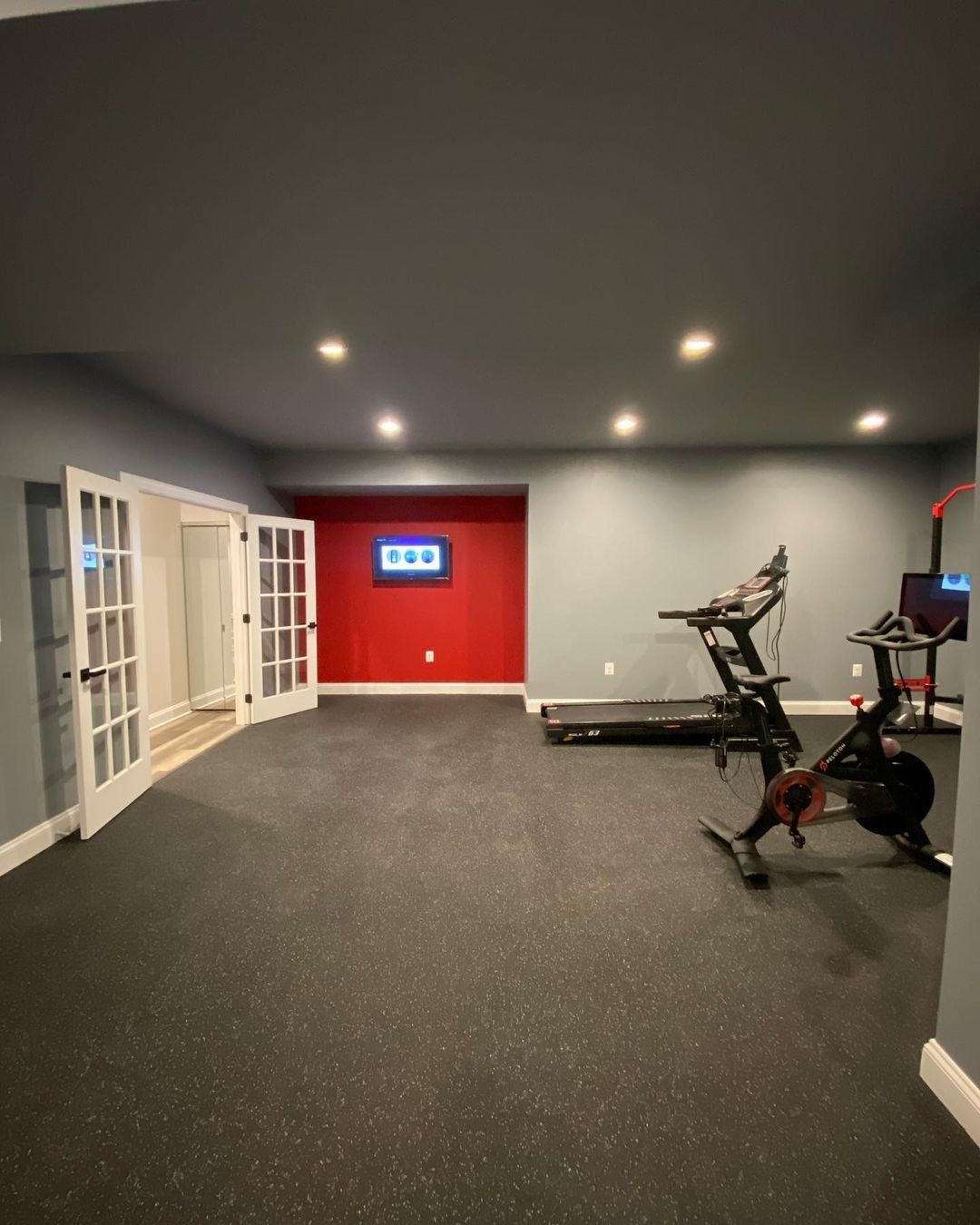 Home gym with dark gray walls, red accent wall, cardio equipment, and French doors.