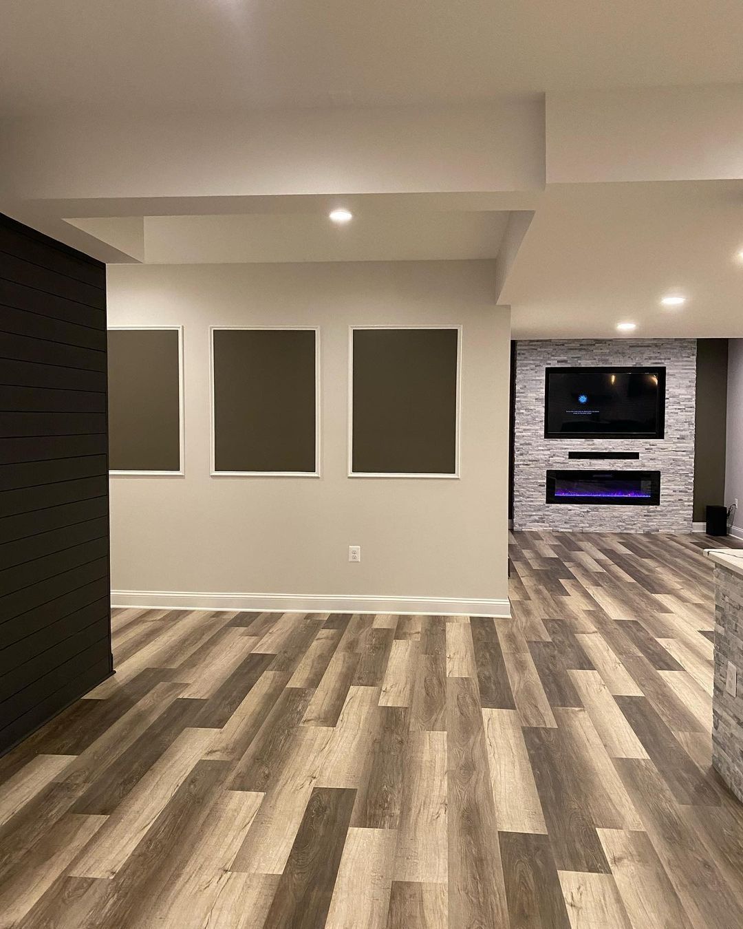 Finished basement with framed art, fireplace, and wood-look flooring.