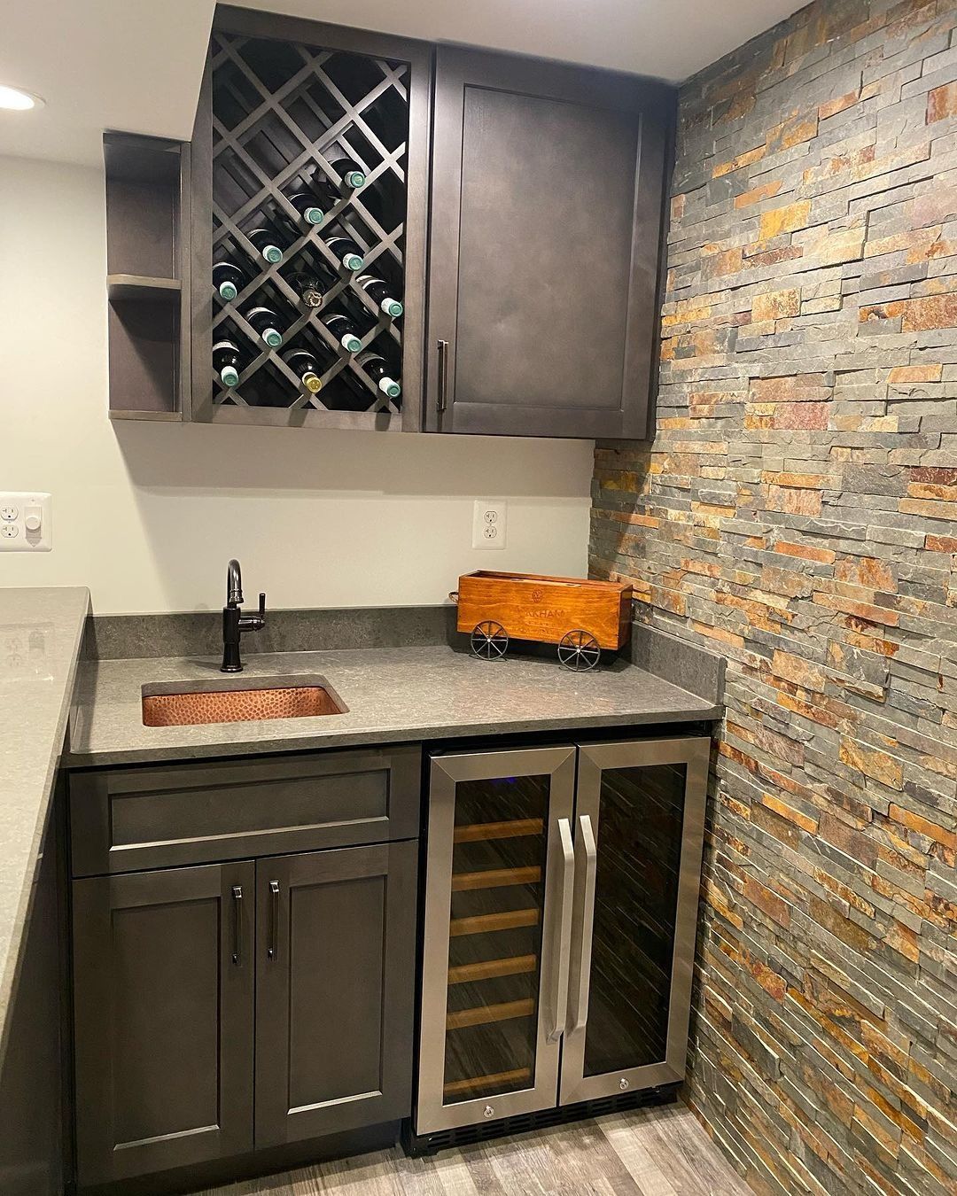Dark-stained wood bar with wine rack, sink, wine fridge, and stone accent wall.