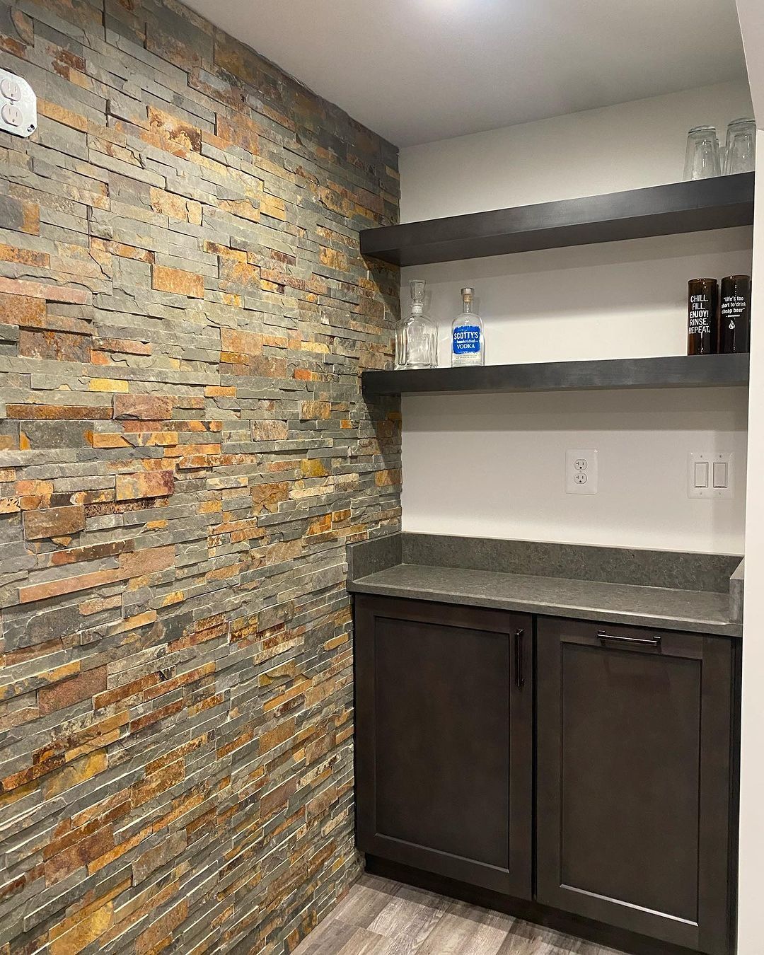 Stone accent wall, built-in bar with cabinets, shelves, and gray countertop.