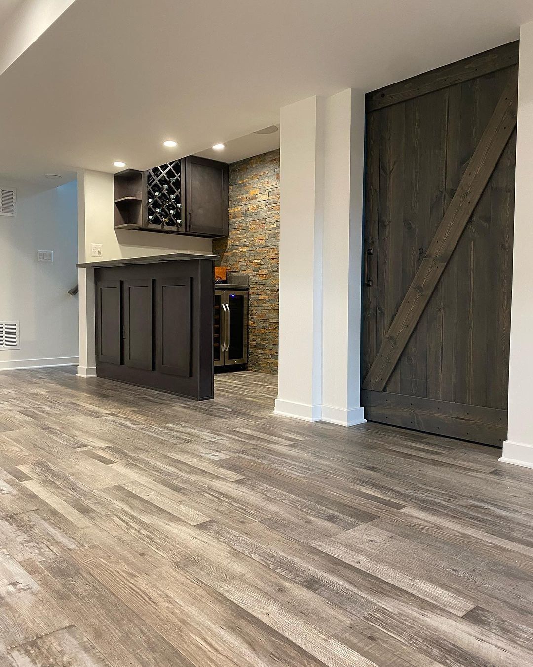 Basement with a dark-stained barn door, wooden floor, and a built-in bar with a stone accent wall.