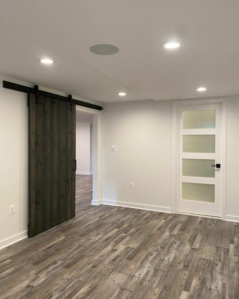 Interior room with dark wood barn door, white door with glass panels, and wood-look flooring.