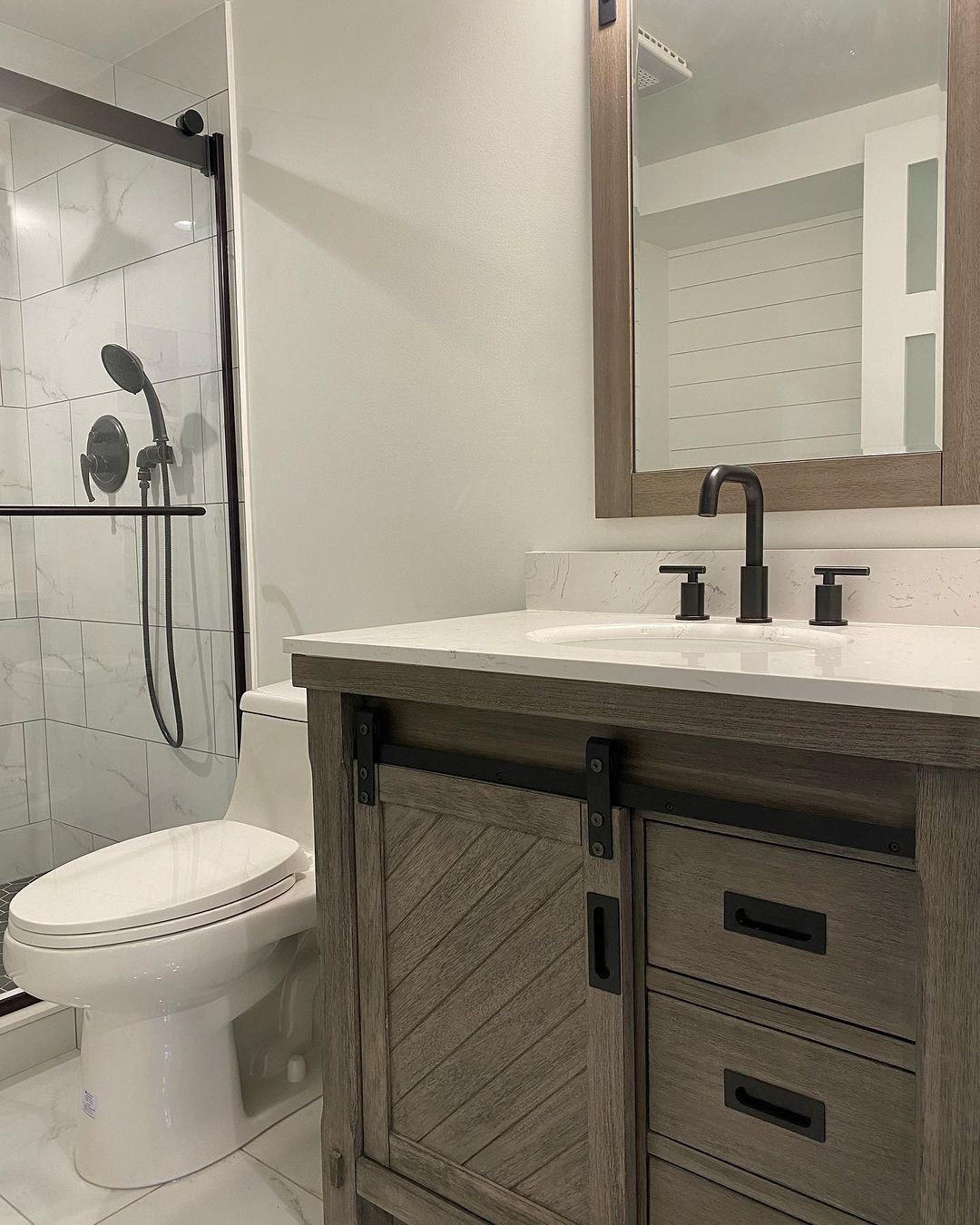 Bathroom with a vanity and a shower, featuring a wooden cabinet and dark fixtures.