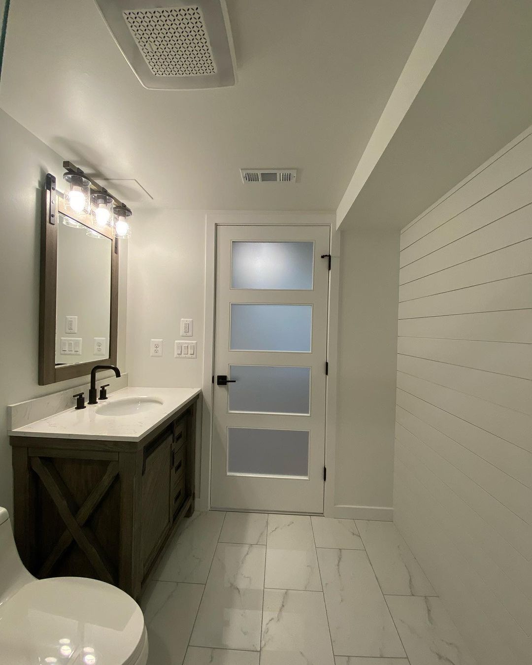 Modern bathroom with white walls, wood vanity, and frosted glass door.