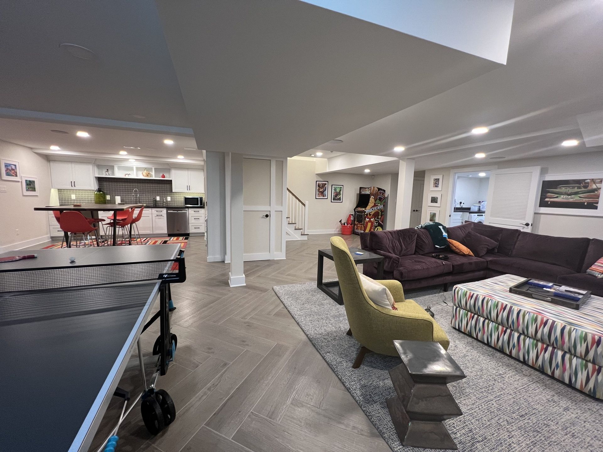 Spacious finished basement with ping pong table, kitchen, seating area, and stairs.