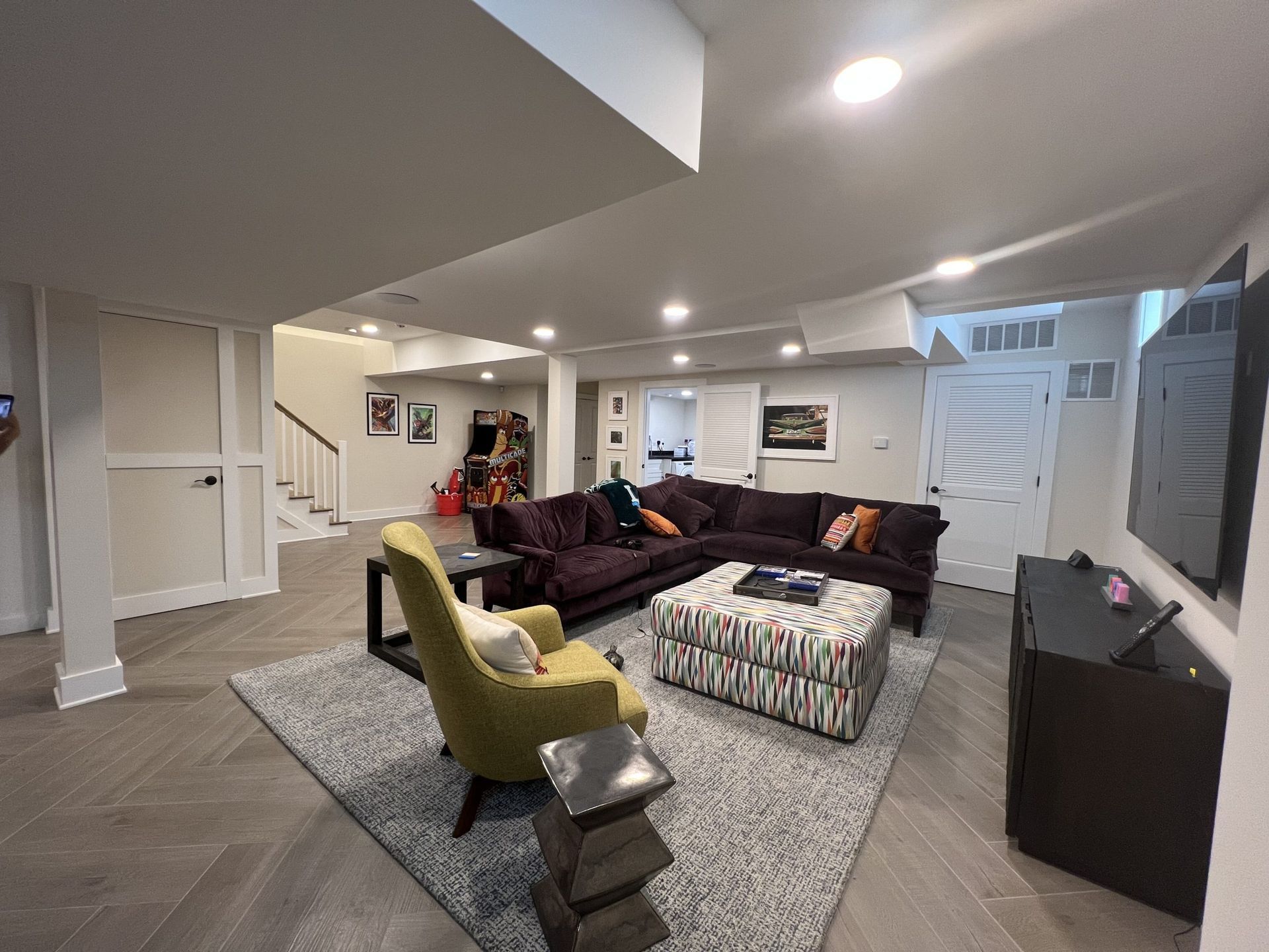 Living room with sectional sofa, armchair, and media cabinet. Neutral color scheme, bright overhead lighting.