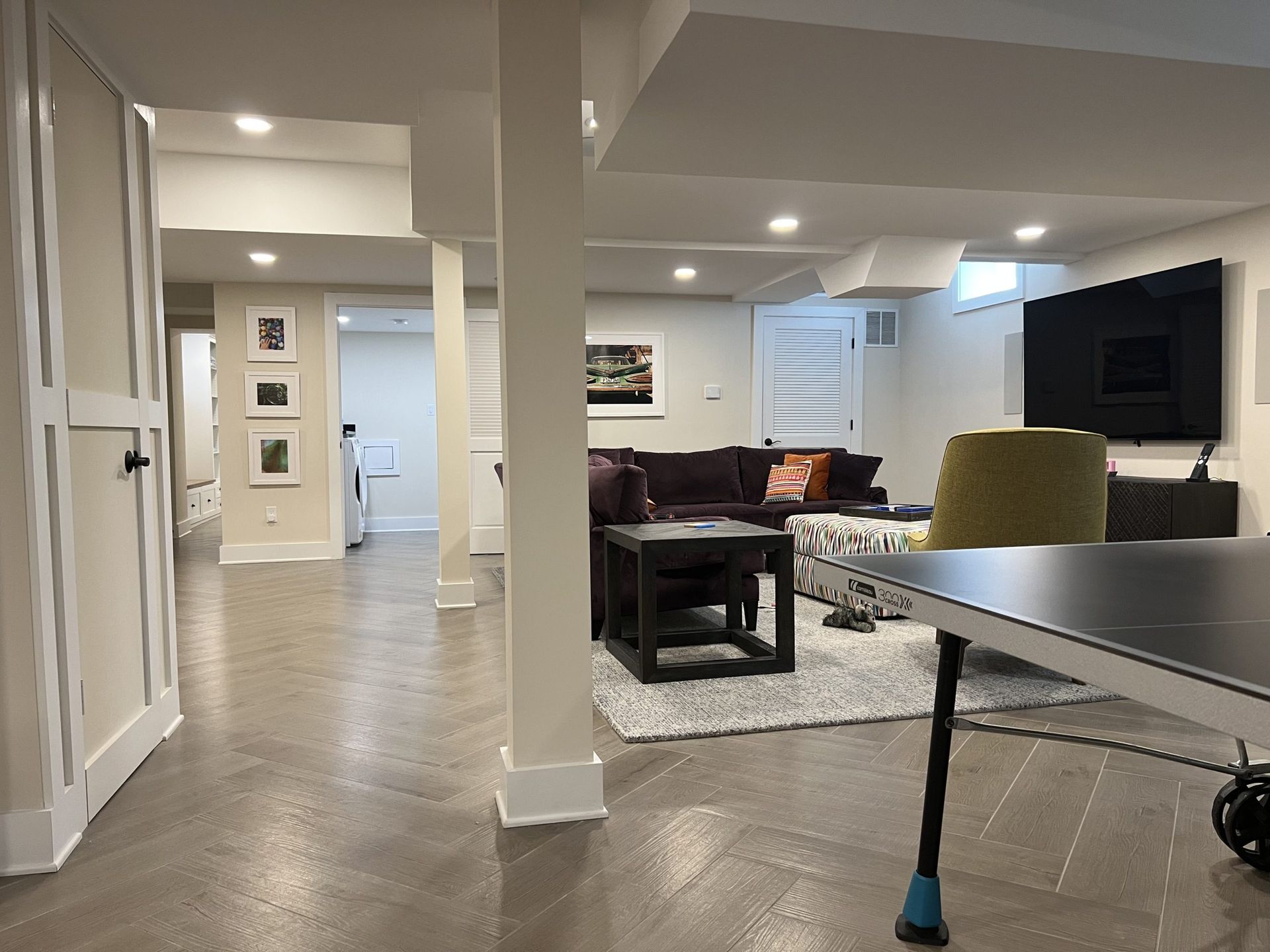 A finished basement with a living area, columns, and a ping-pong table.