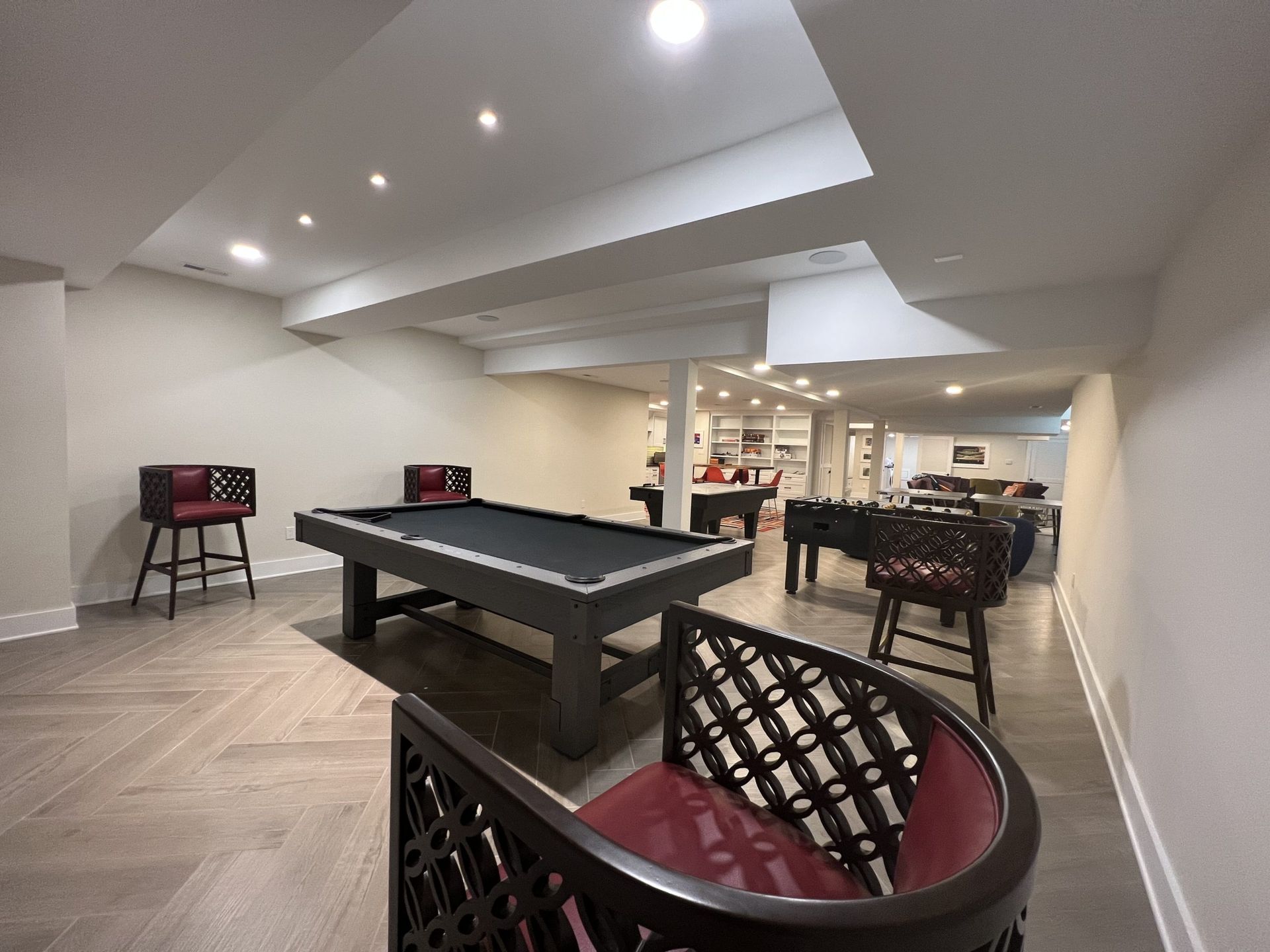 A finished basement with a pool table, bar stools, and a foosball table. Neutral tones.