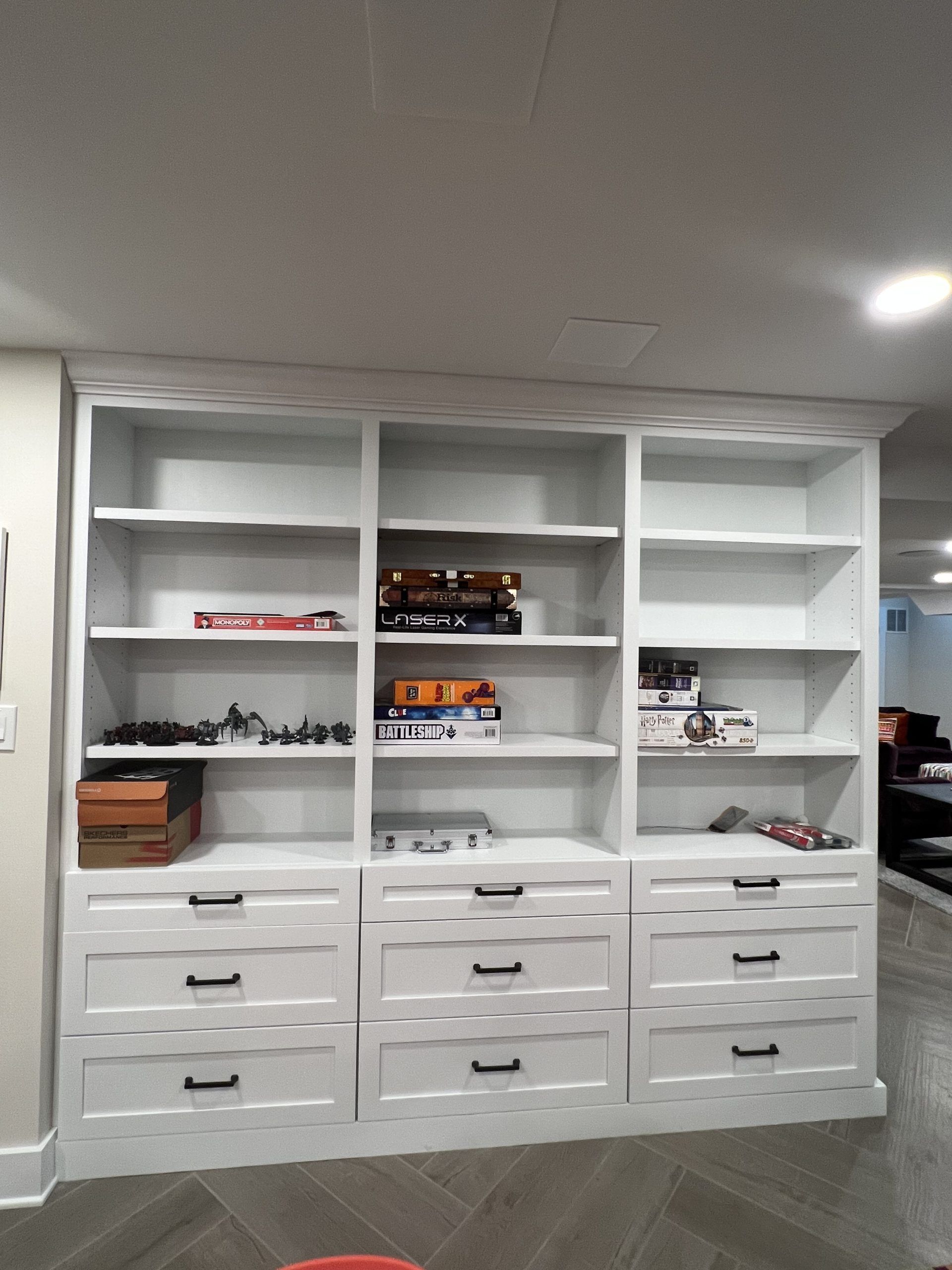 White built-in bookshelf with three sections, shelves above drawers, storing items in a basement.