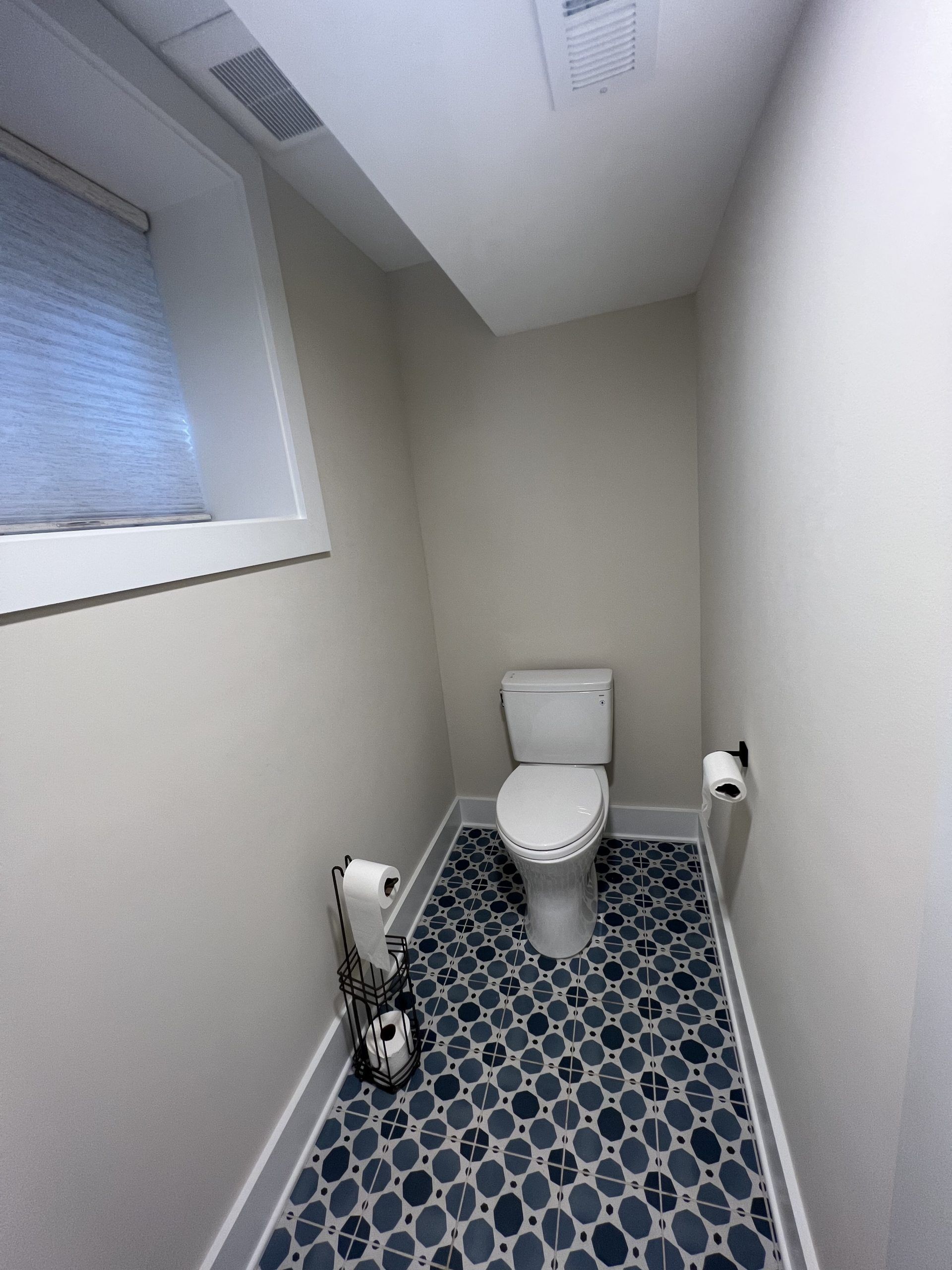 A small, modern bathroom with a toilet, blue patterned floor, and two rolls of toilet paper.