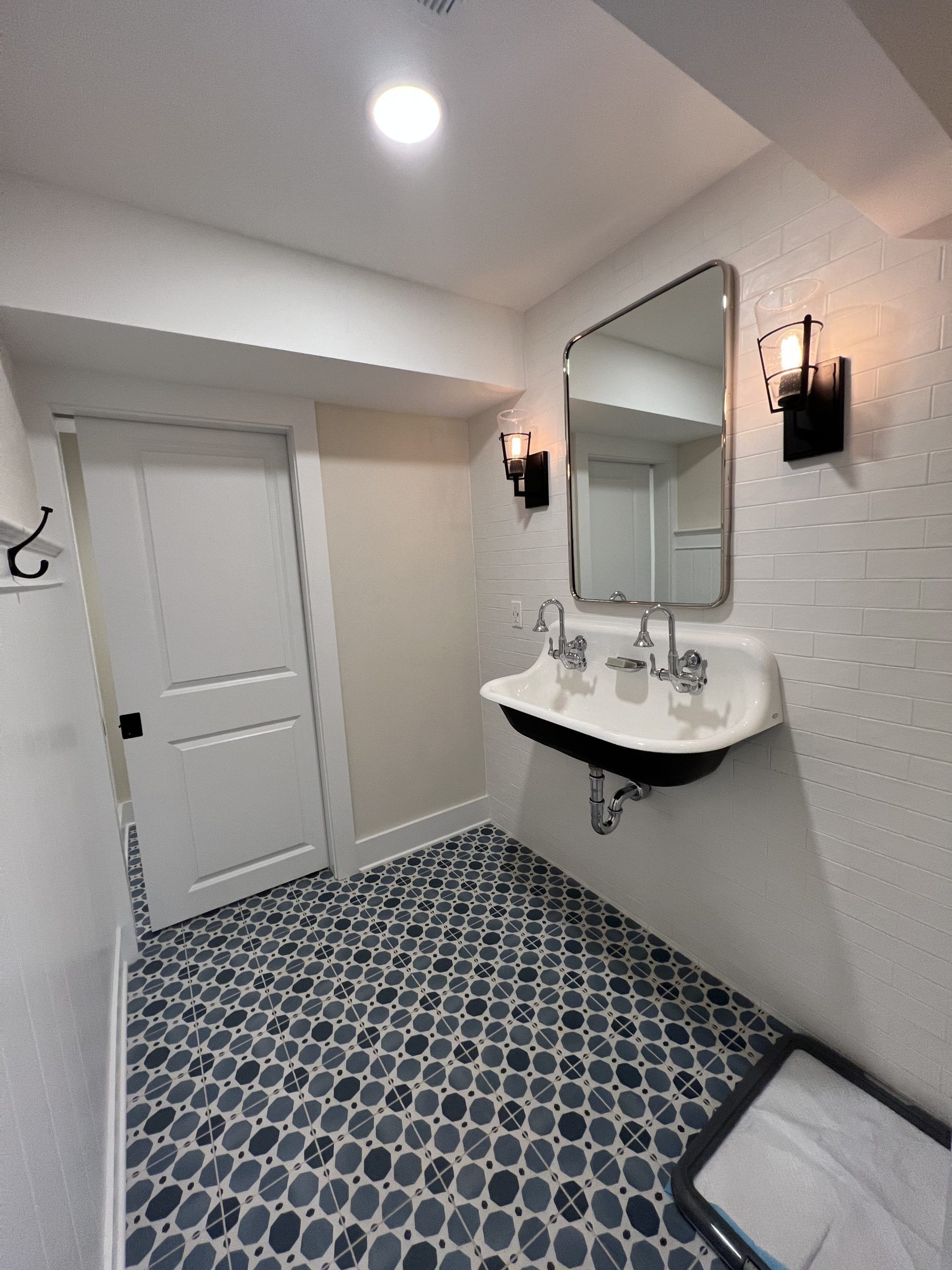 Small bathroom with patterned floor, white walls, and a vintage-style sink and mirror.