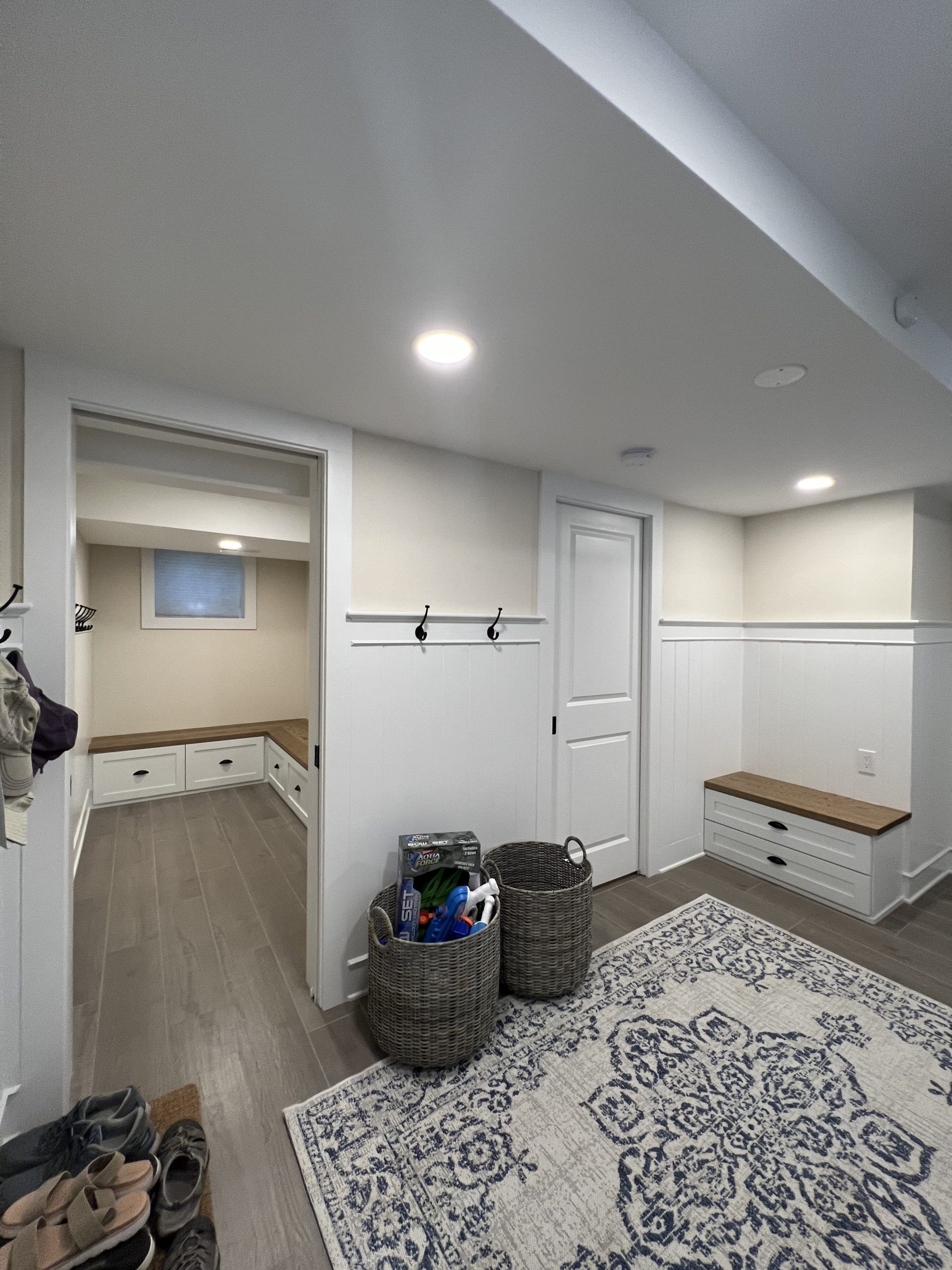 Entryway with gray floors, white walls, storage benches, door, rug, baskets, and hooks.