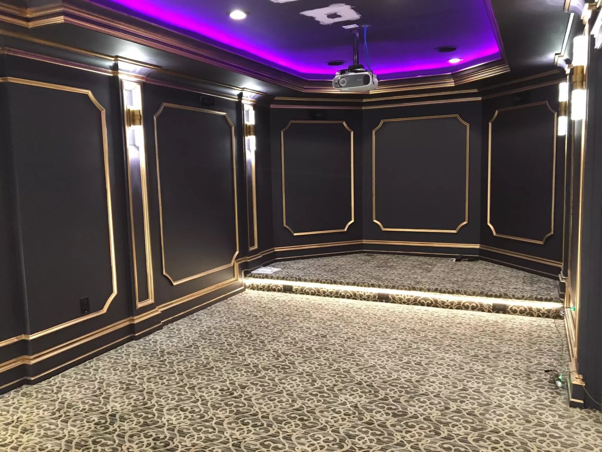 Dark home theater with gold trim, purple ceiling lights, and patterned carpet.