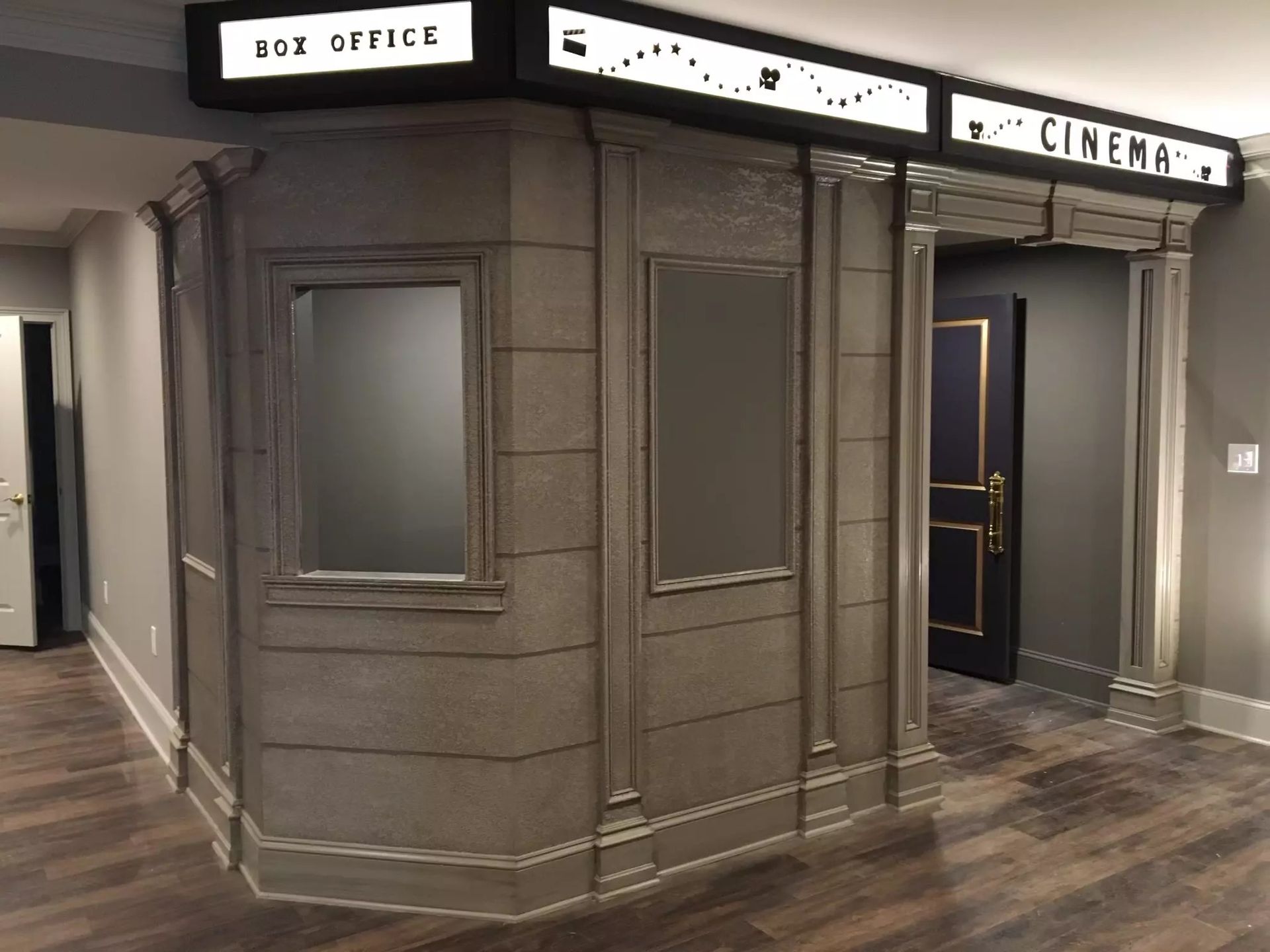 A faux movie theater box office with illuminated signs and a door to a cinema.