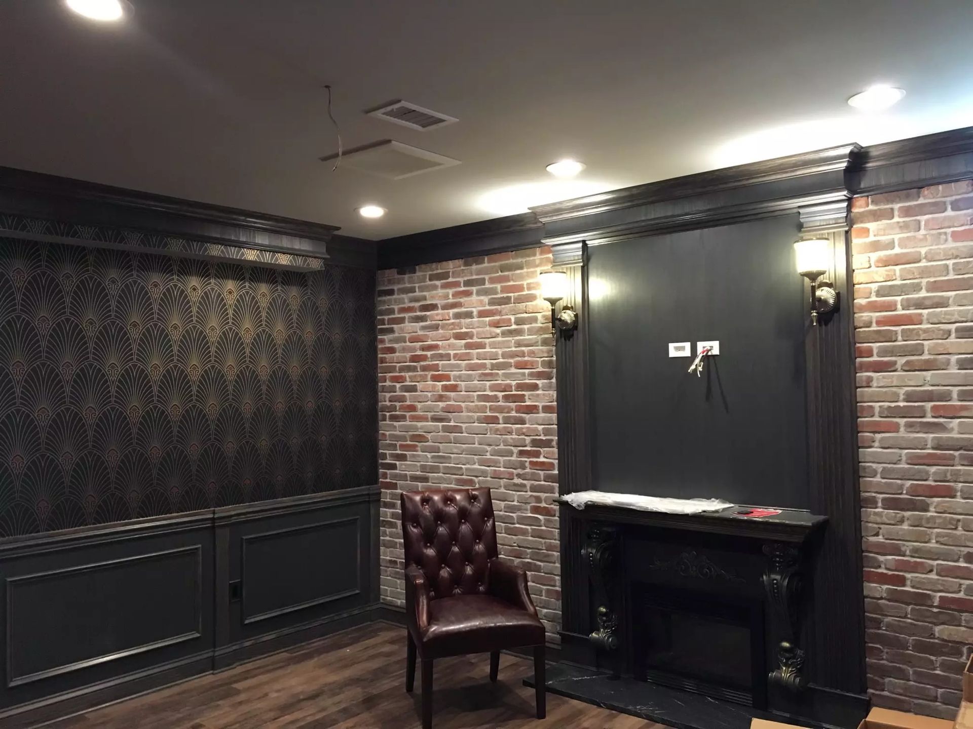 Room with brick and patterned wallpaper walls, dark trim, a fireplace, and a leather chair.