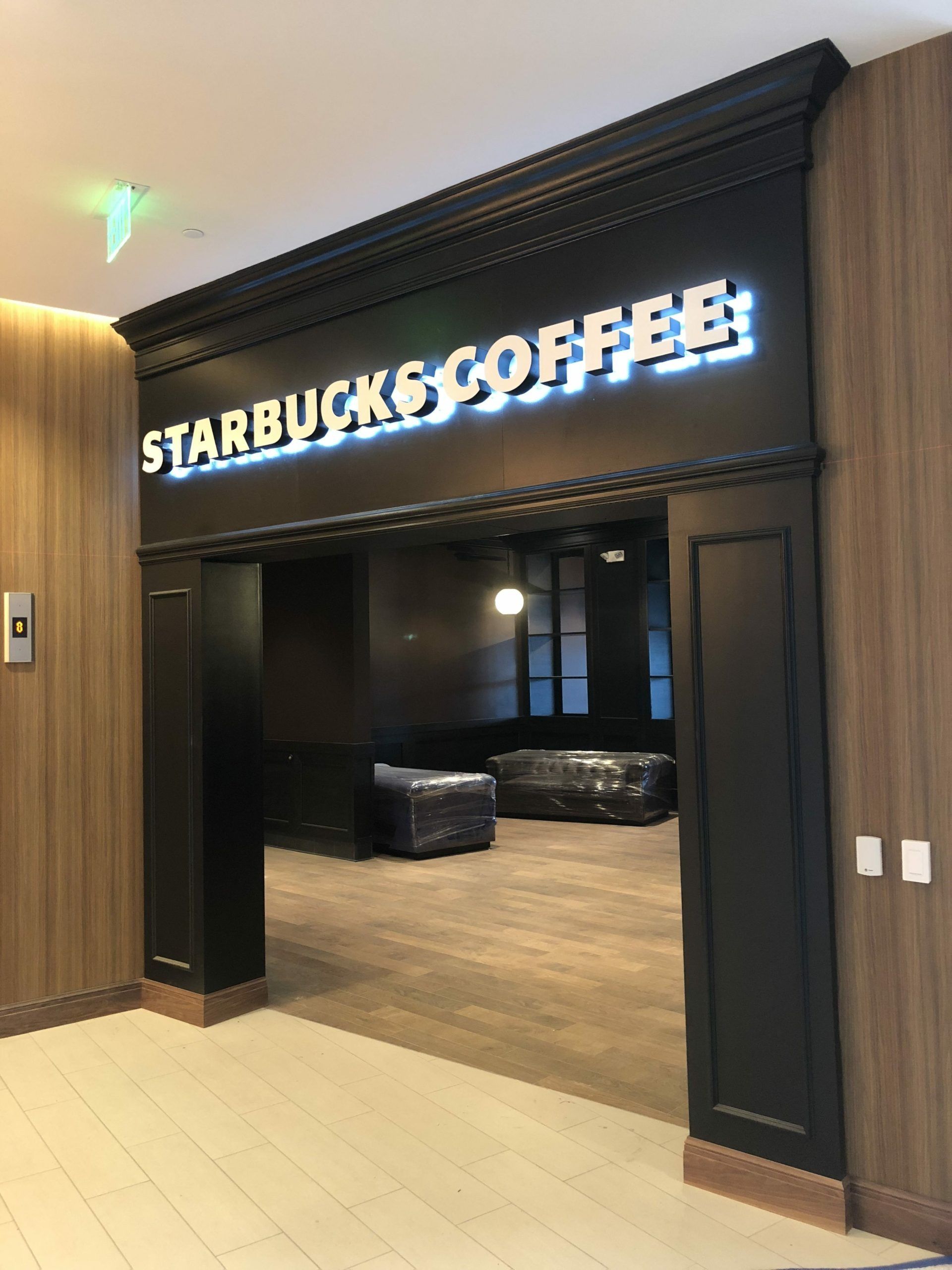Starbucks & Coffee shop entrance with illuminated sign. Dark doorway, wood paneling, light flooring.