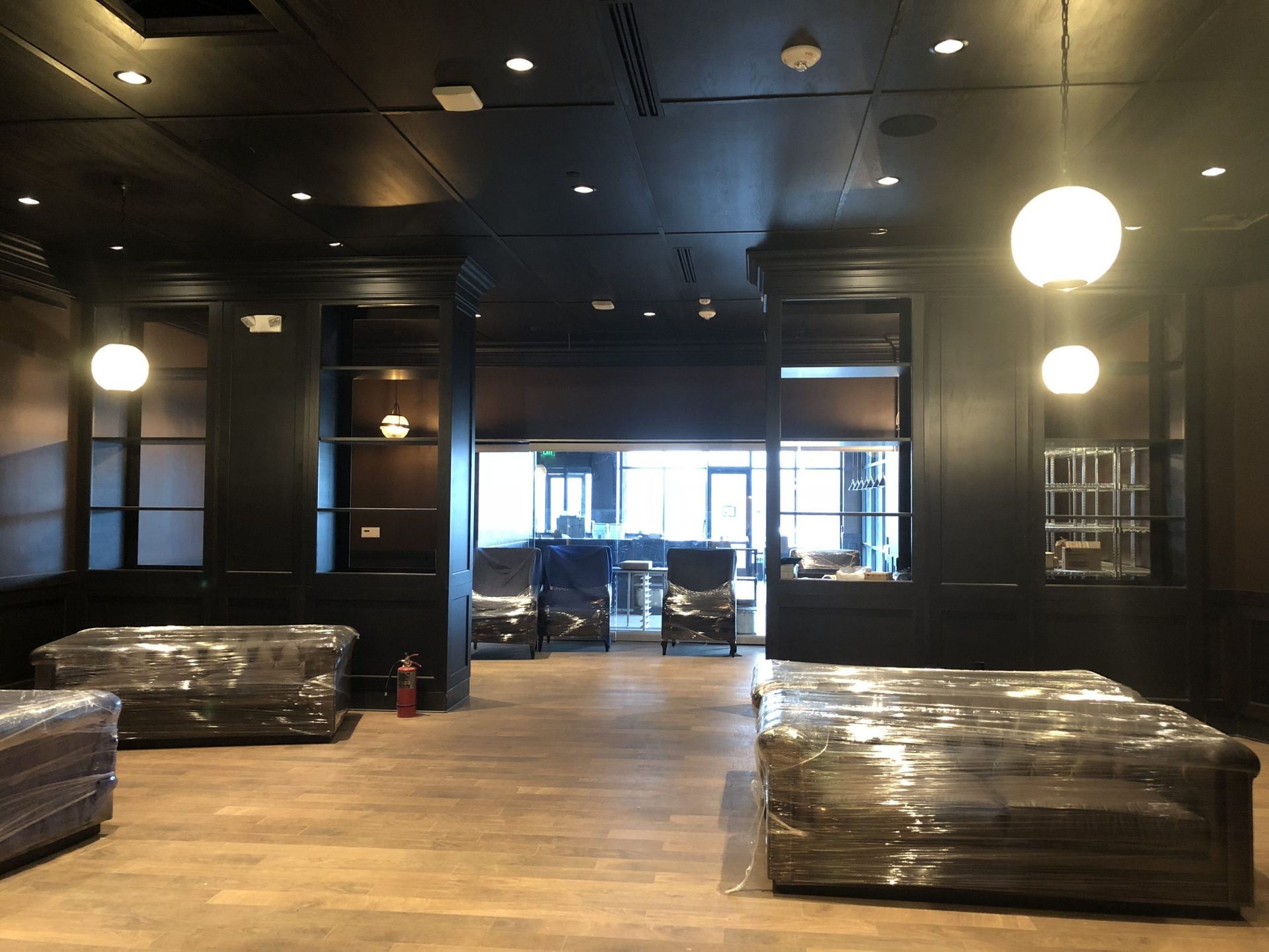Dark-toned room with wrapped furniture, open doorway to exterior, globe pendant lights.