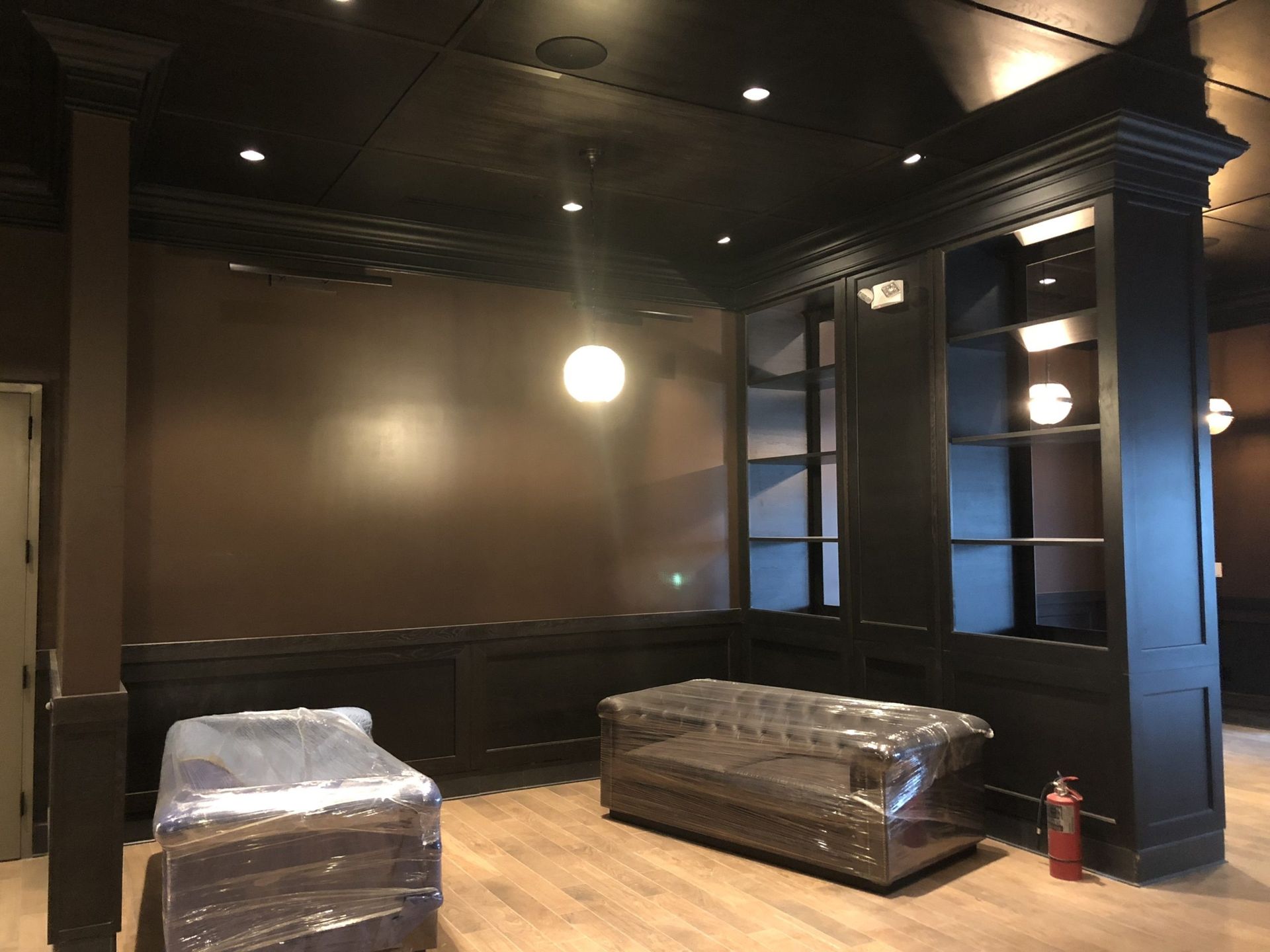 Dark-paneled room with a sofa and armchair in plastic, built-in shelving, and wood flooring.
