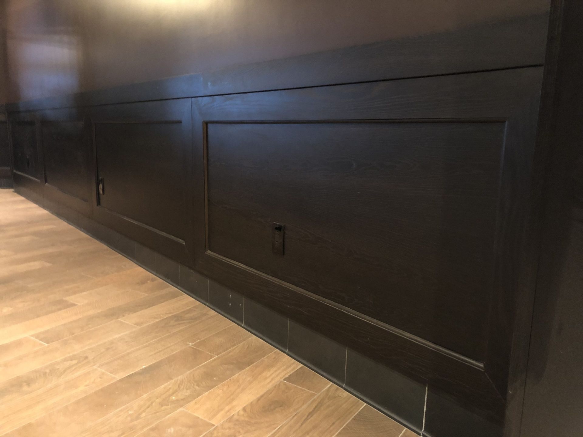 Black cabinet doors with handles set into a wall above light wood flooring, dark trim.