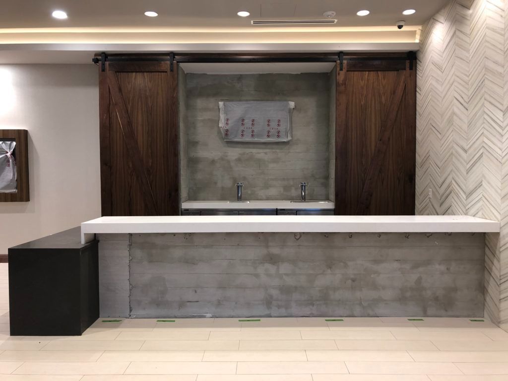 Bar with wooden doors, concrete accents, white countertop, and patterned wall.