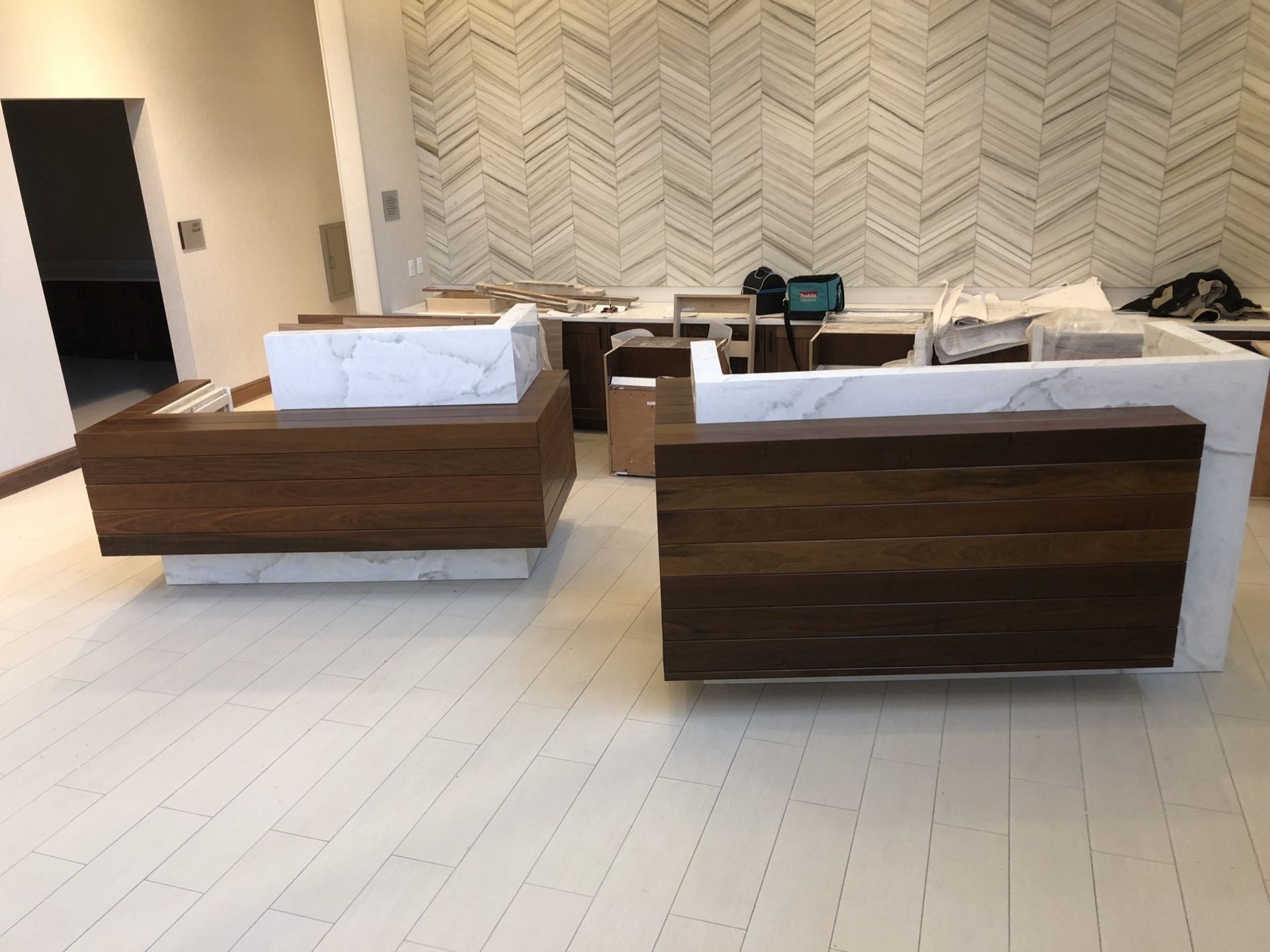 Two modern wooden reception desks with white marble tops on light-colored flooring in a room with a patterned wall.