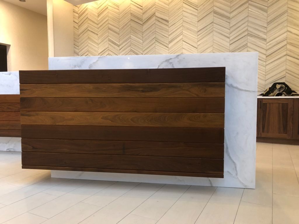 Wooden front desk with marble sides, set against a zig-zag patterned wall.