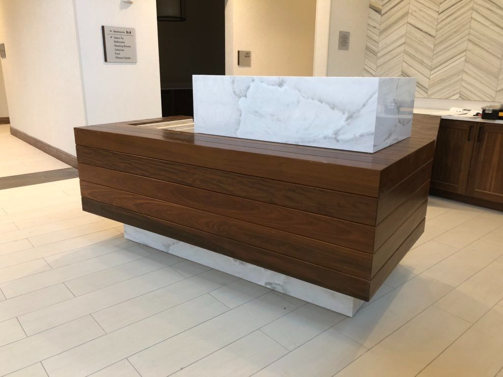 A modern, wood-paneled reception desk with a white marble top in a lobby.