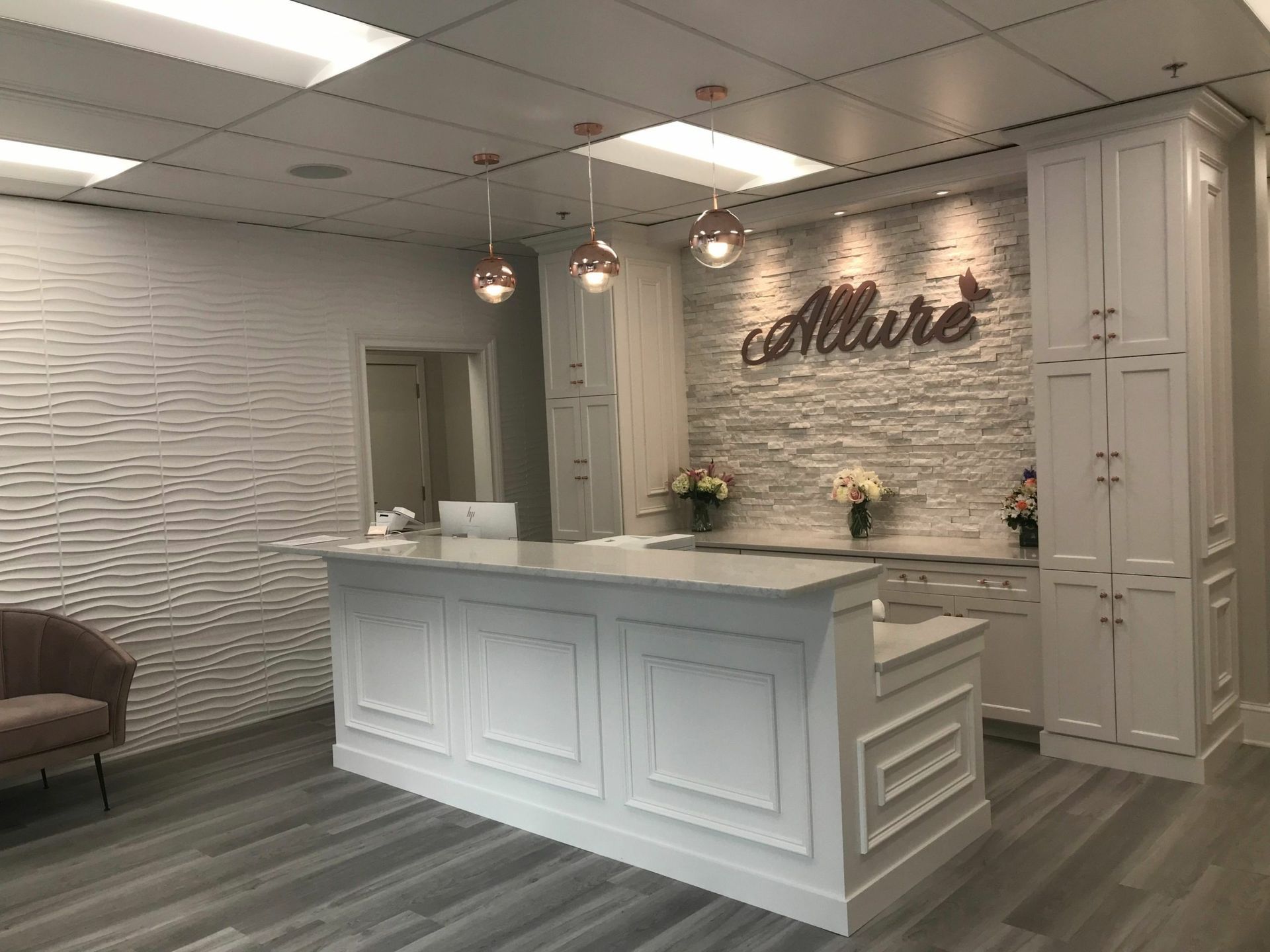 Reception area of a business, white and gray decor with a reception desk, floral arrangements, and pendant lights.