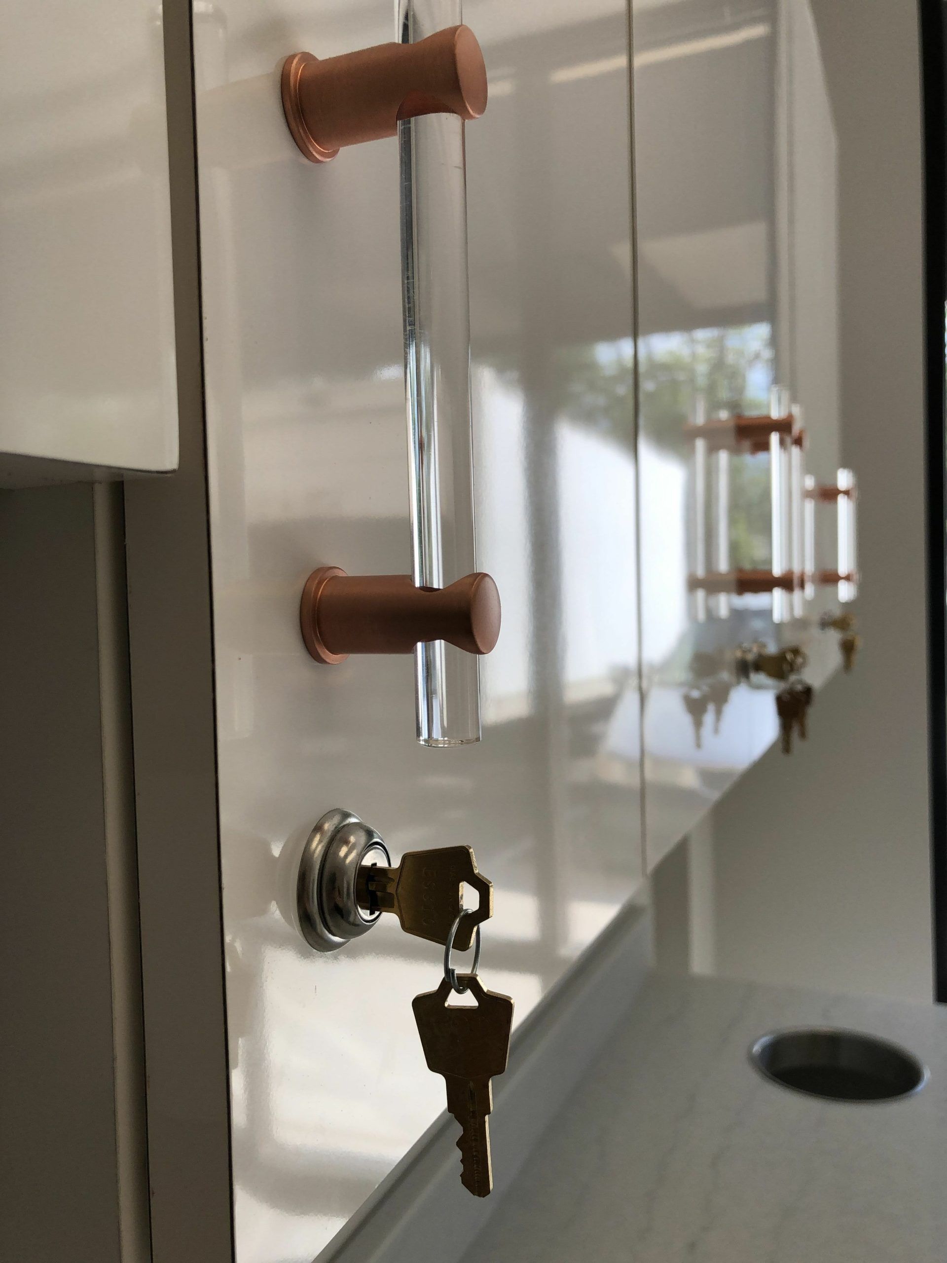 White cabinet with copper pulls, clear handles, and a lock with a key.