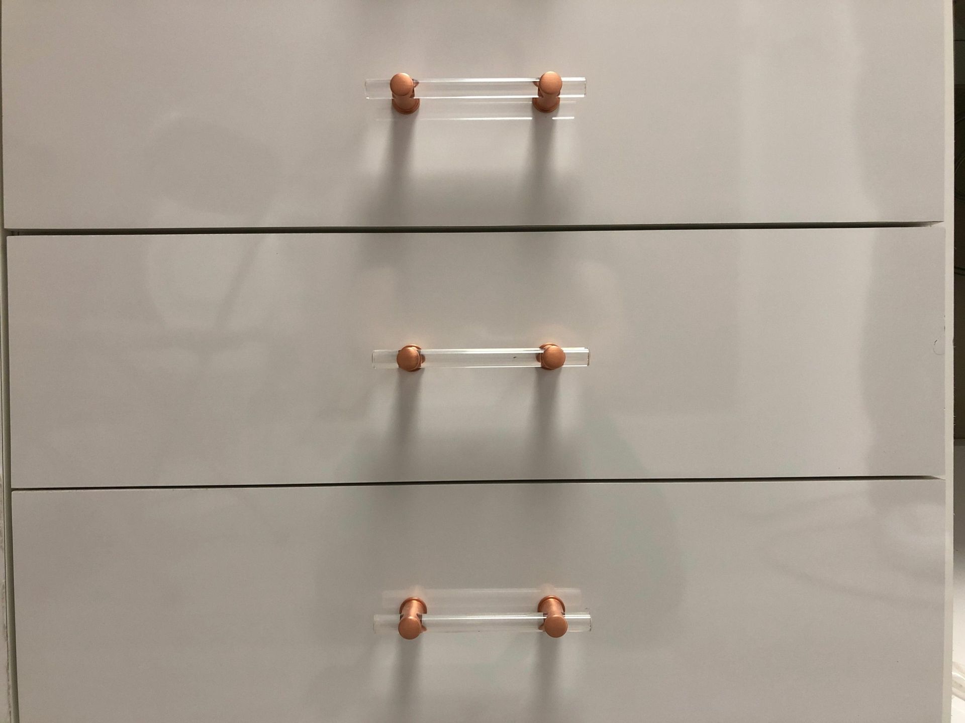 Three white dresser drawers with clear acrylic and rose gold hardware.
